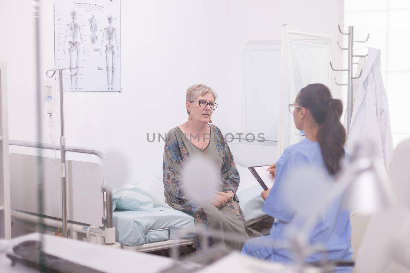 Nurse taking notes during consultation of senior woman in doctor hospital cabinet. Elderly woman talking with assistant.