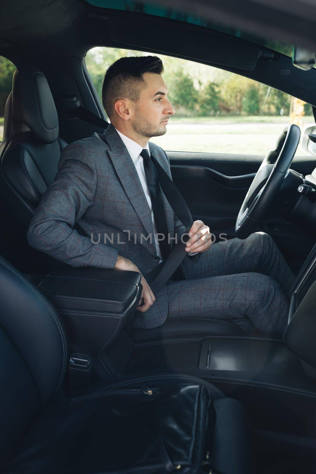 Handsome young man pinches seat belt and riding happily smiling. Joyfull driver. Lifestyle, road, car, driver concept. Protection of a person in vehicles. Road safety regulations concept. by uflypro