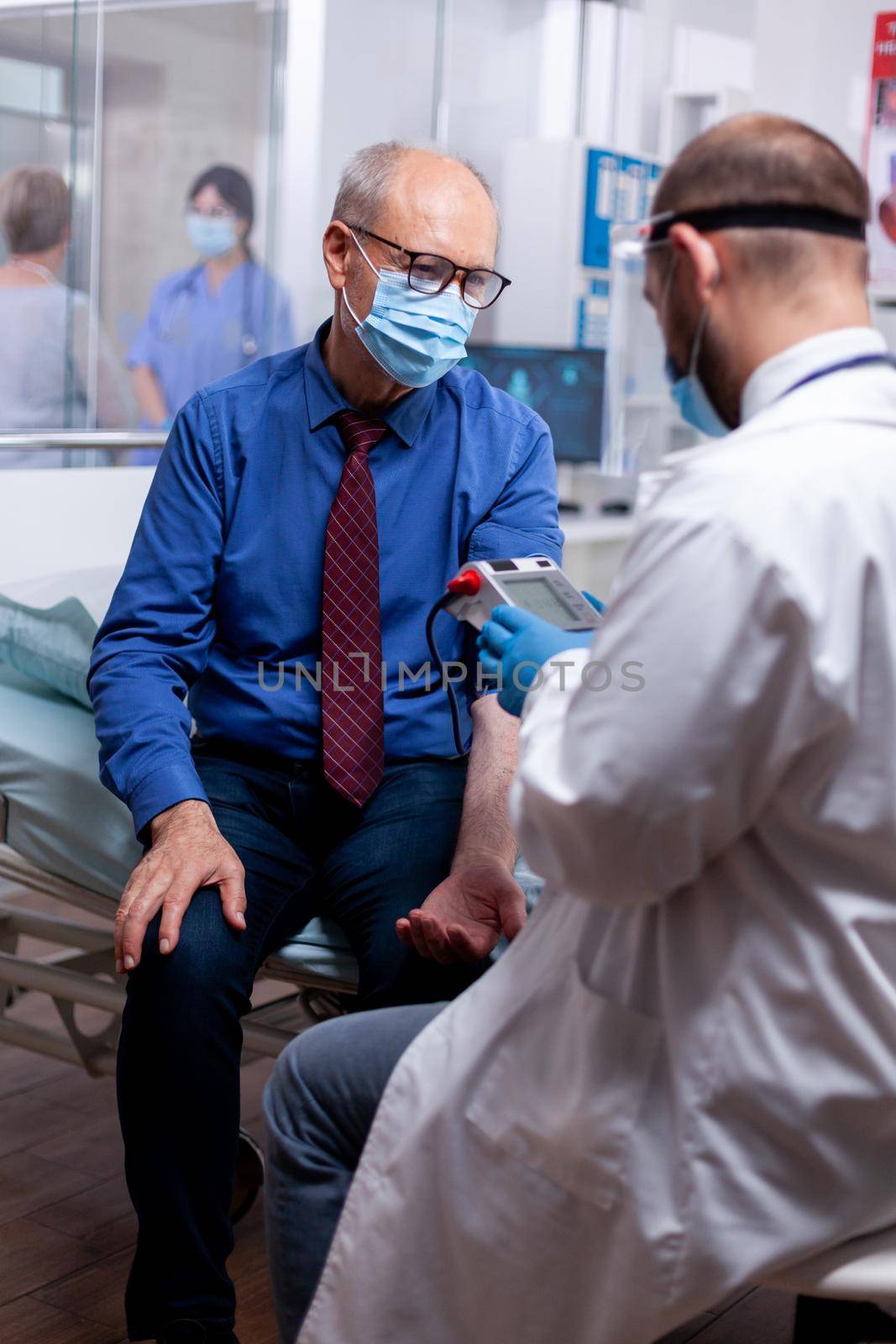 Doctor with protective mask against coronavirus measuring blood pressure of elderly man in hospital. Medical examination for infections, disease and diagnosis.