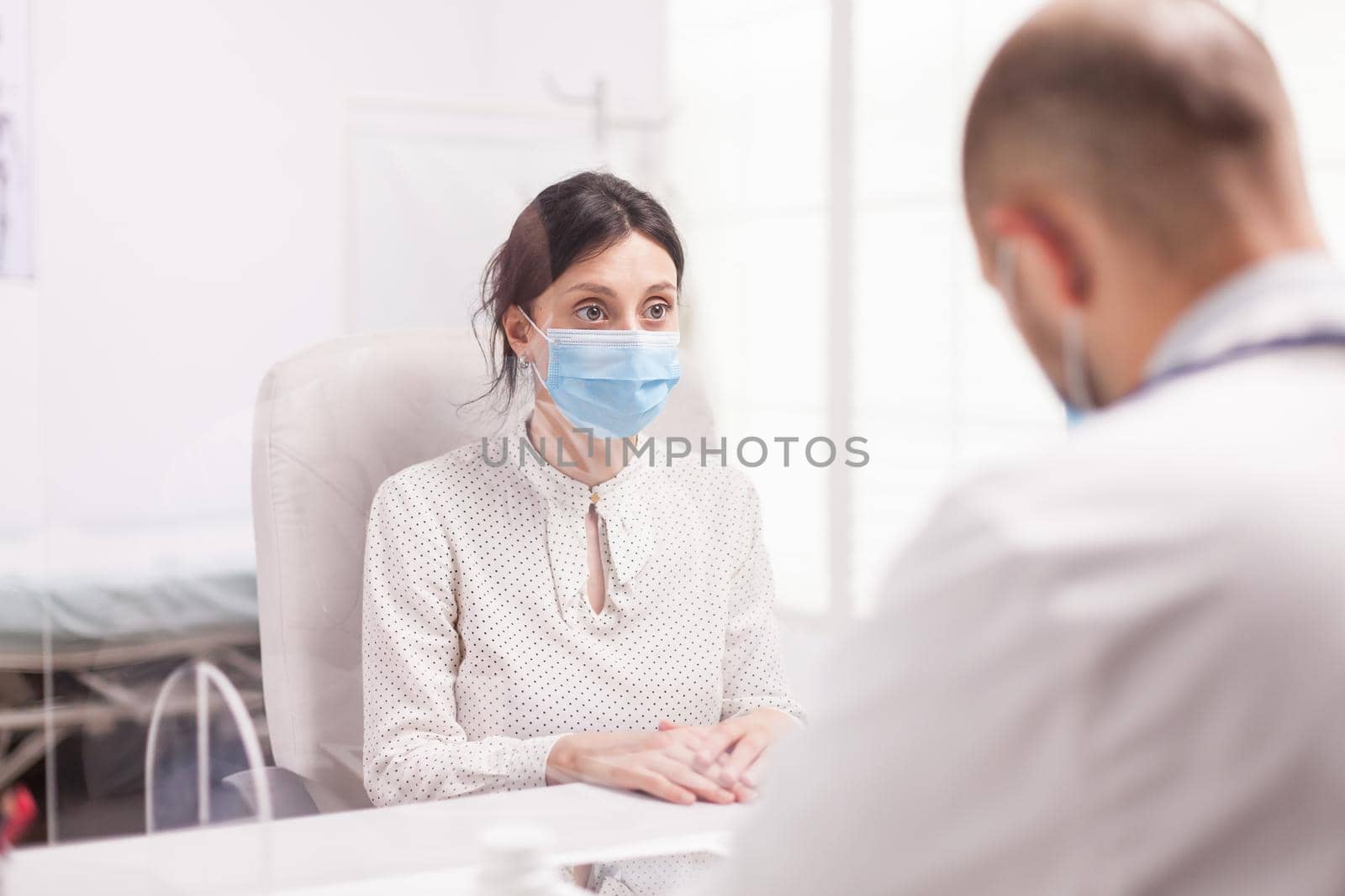 Sick woman wearing protection mask against coronavirus during examination with doctor in hospital office.