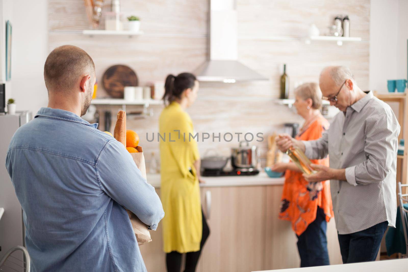 Man arriving home with grocery paper bag from supermarket. Happy big family prepearing tasty brunch. Senior man holding bottle of wine.