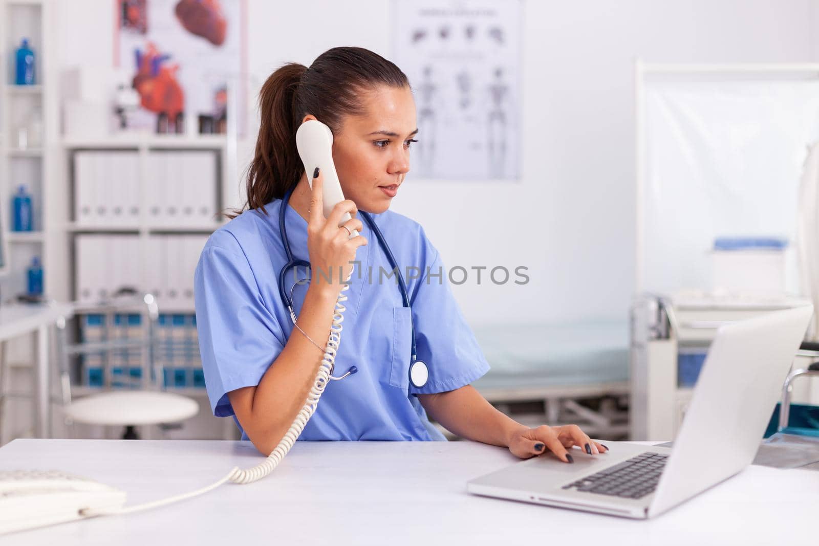 Medical practitioner answering phone calls and scheduling appointments in hospital office. Health care physician sitting at desk using computer in modern clinic looking at monitor.