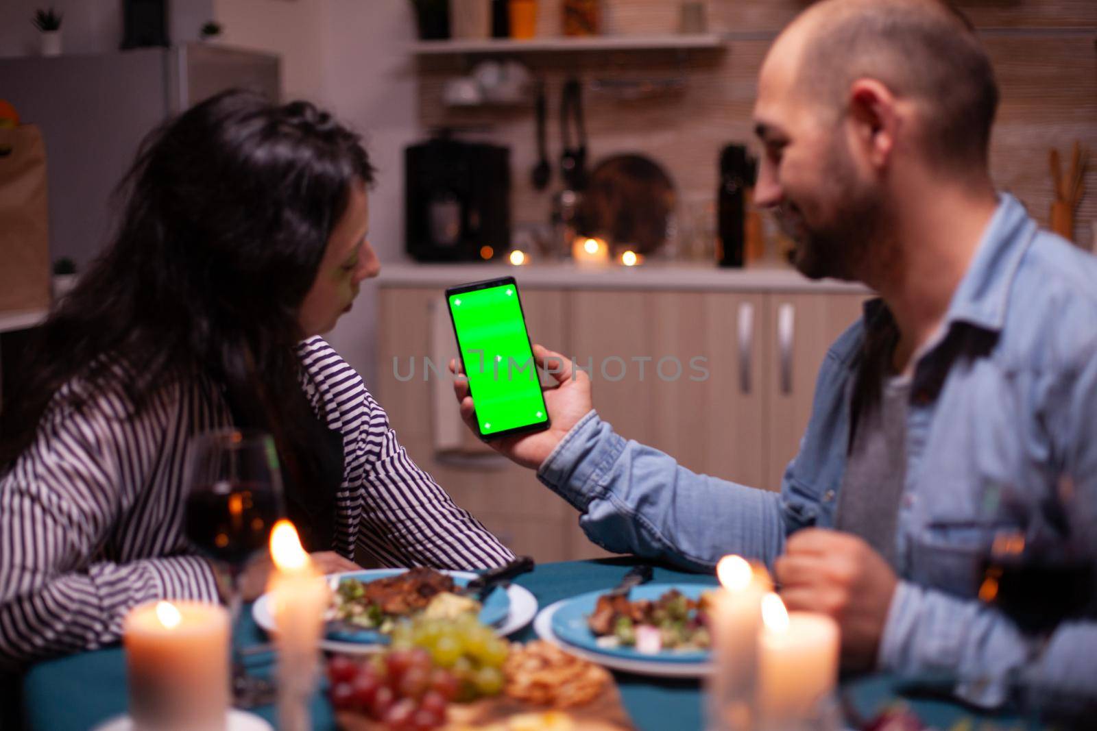 Couple looking at phone with green mock up having romantic dinner. Happy holding phone green screen template chroma key isolated smartphone display using technology internet.