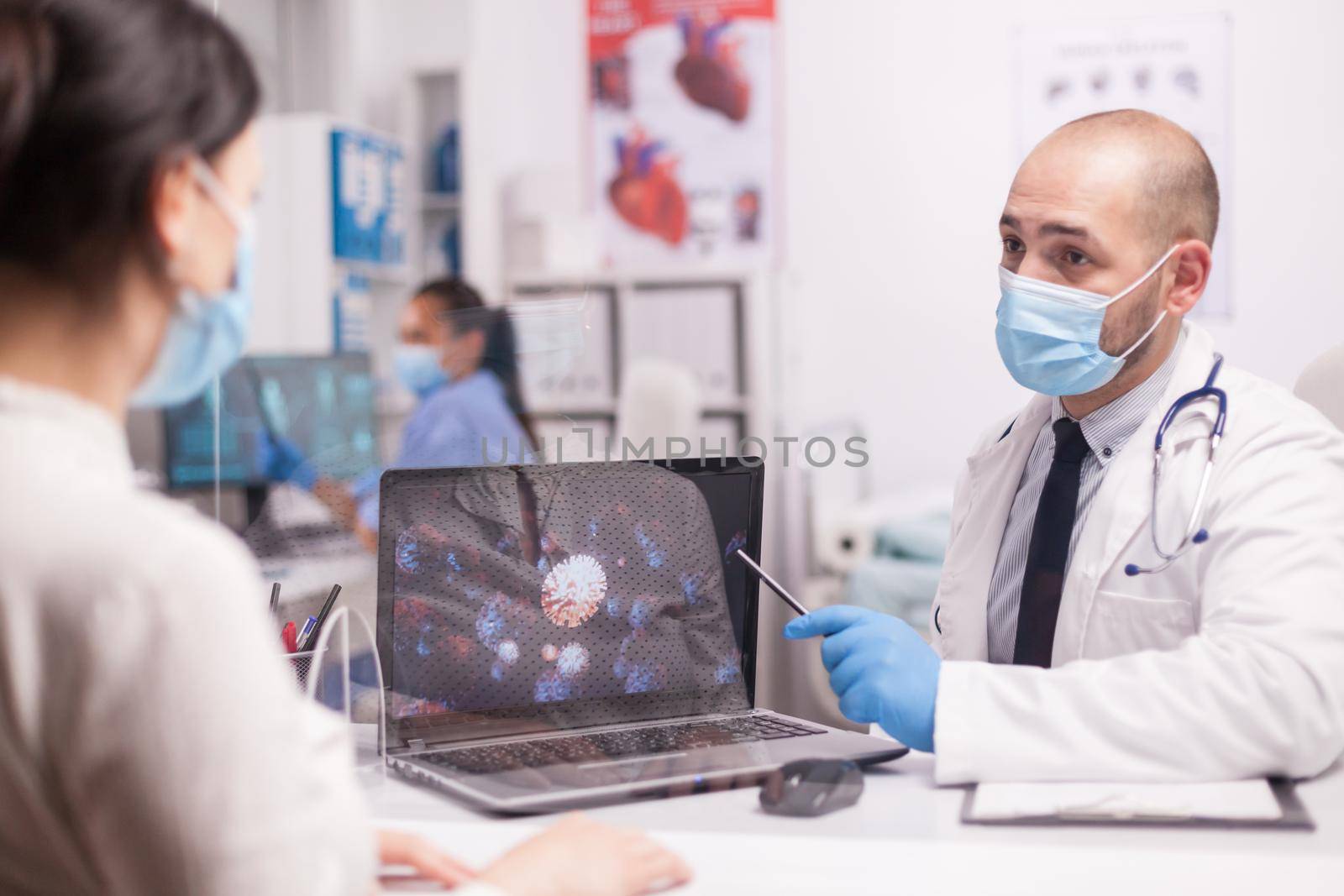 Doctor with mask showing covid-19 animation on laptop during patient examination.