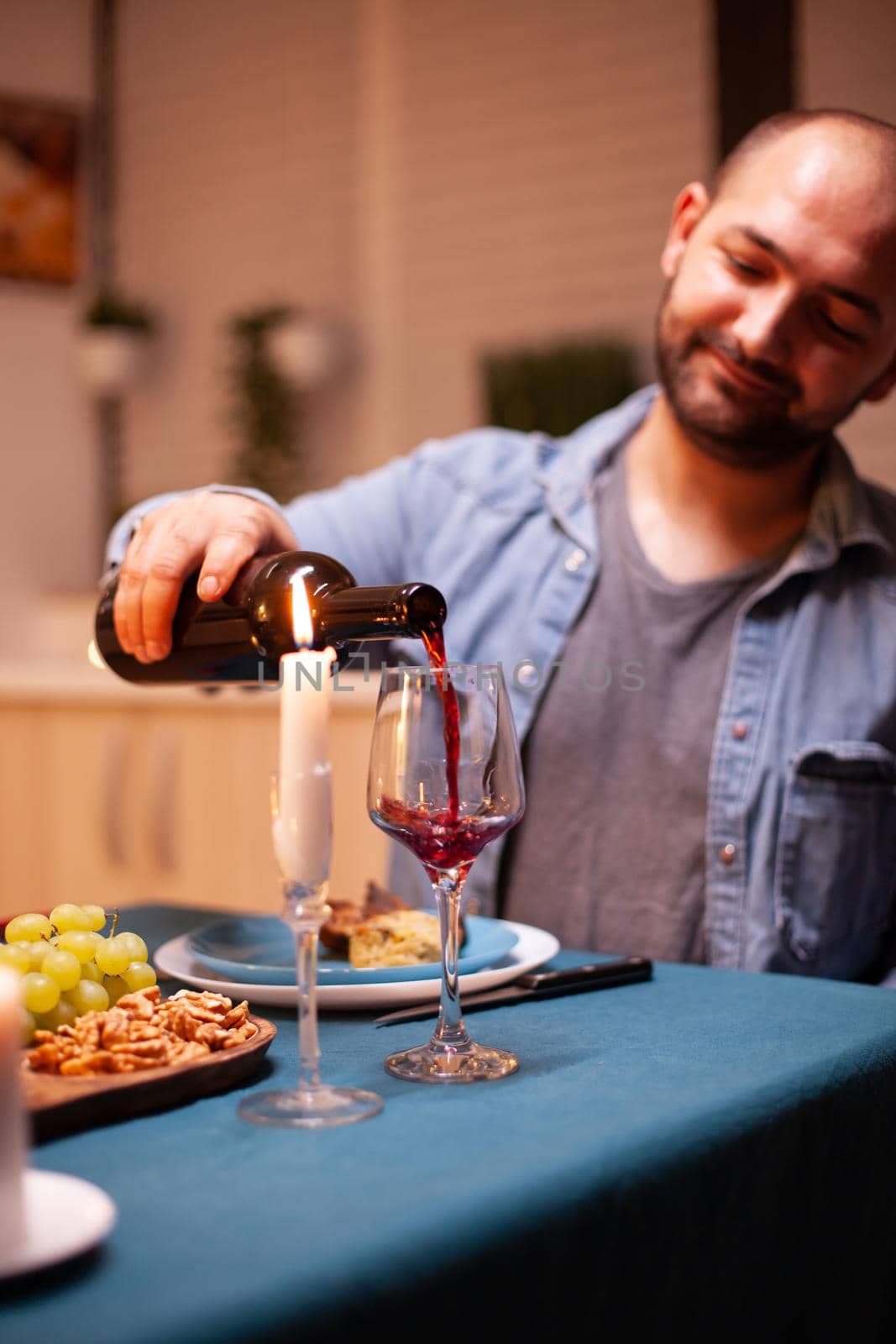 Husband pouring red wine in glass celebrating relationship with wife in dining room. Young man pouring red wine in wife glass. Romantic caucasian happy couple sitting at the table celebrating .