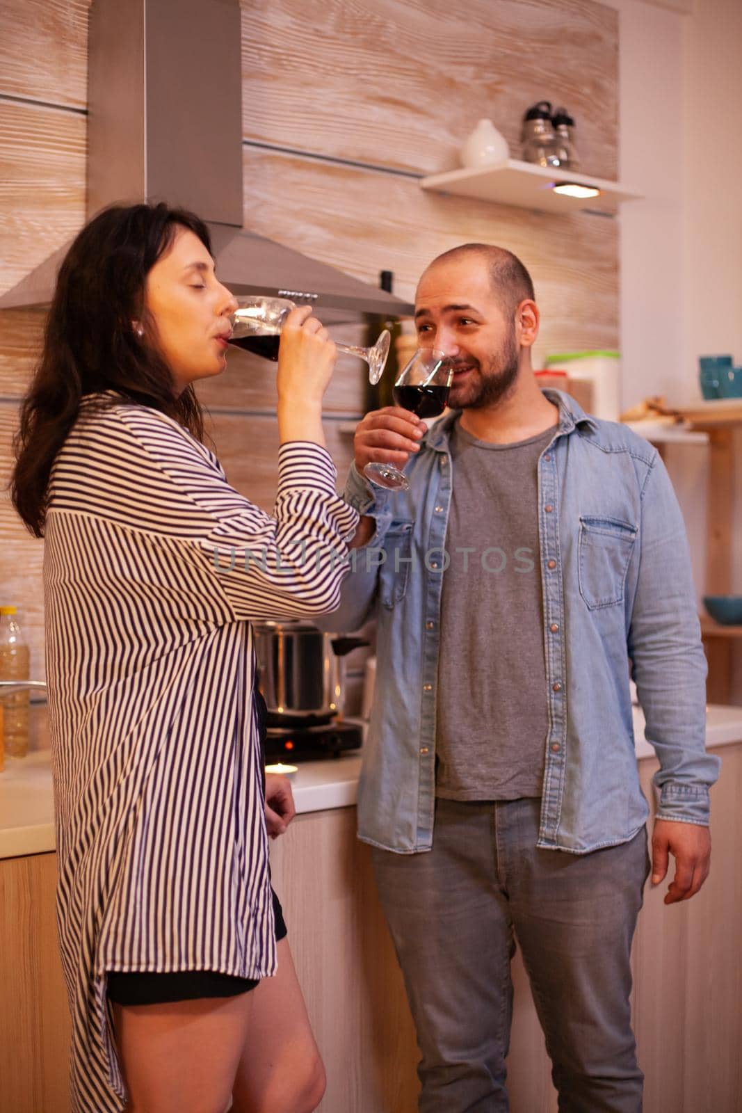 Positive man and woman drinking wine in home. Adult couple having romantic date at home, talking, smiling, enjoying the meal in dining room. Looking at wife.