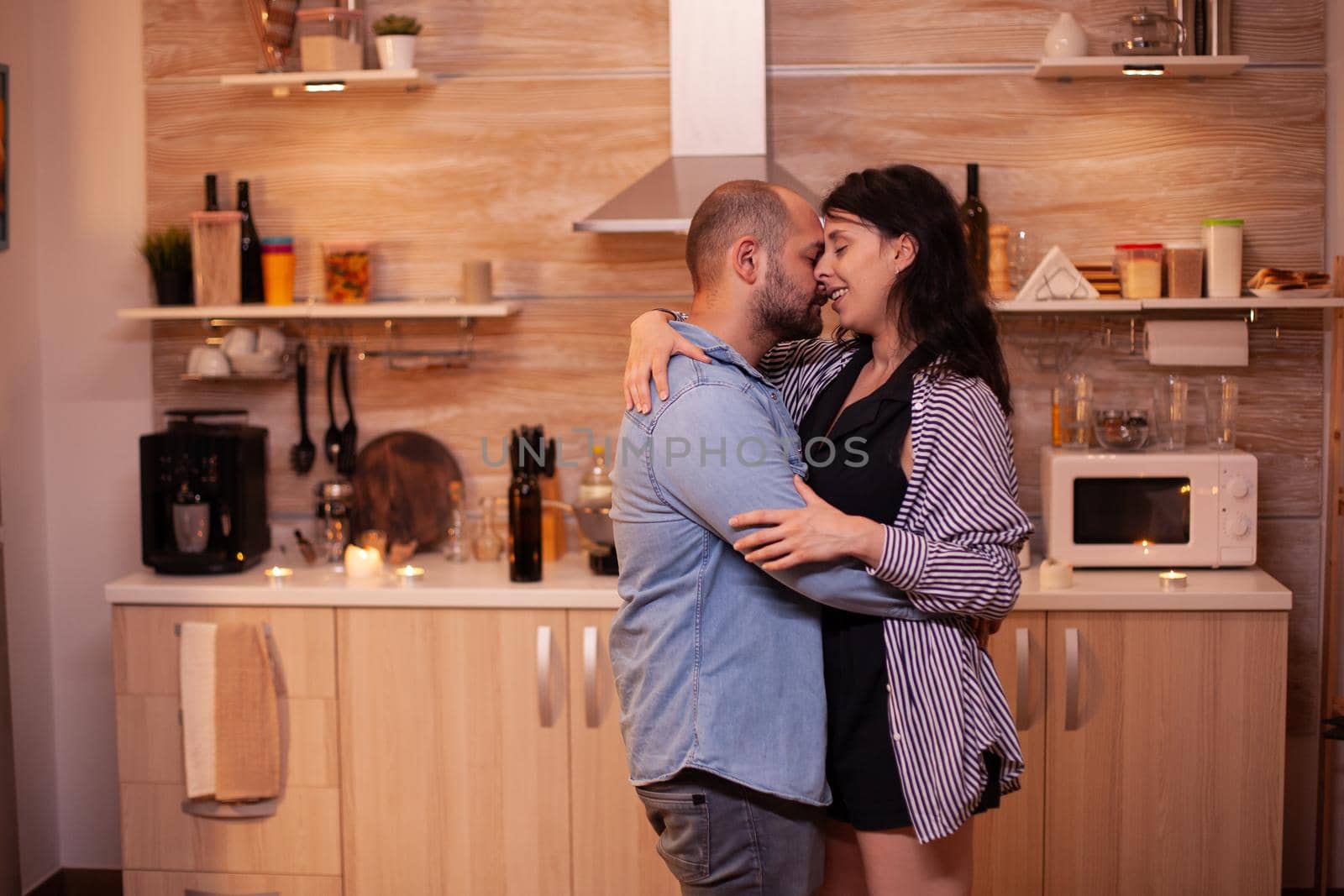 Husband hugs wife during relationship celebration. Happy in love couple dining together at home, enjoying the meal, smiling, having fun, celebrating their anniversary.