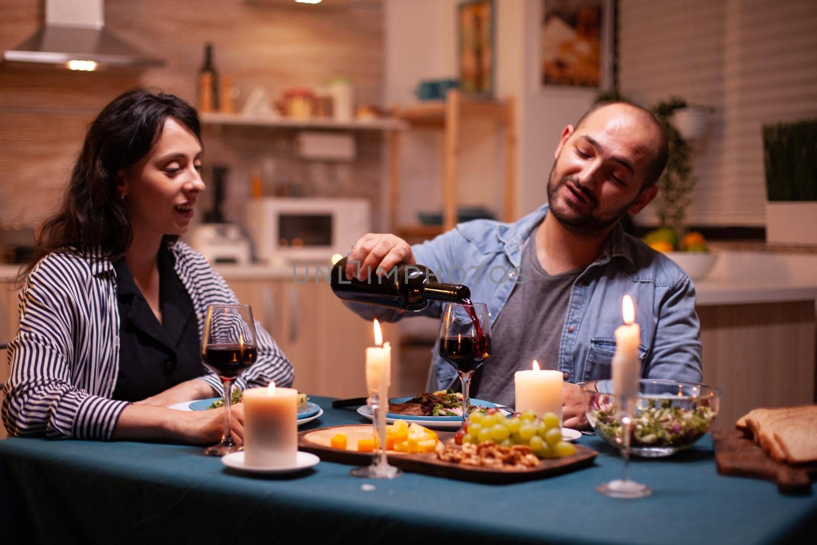 Husband pouring wife to wife during romantic dinner in dining room. young man pouring red wine in wife glass. Romantic caucasian happy couple sitting at the table celebrating .