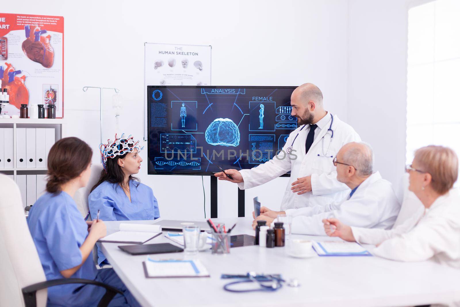 Female nurse wearing scaning headset for brain activity during experiment and doctor telling diagnosis. Monitor shows modern brain study while team of scientist adjusts the device.