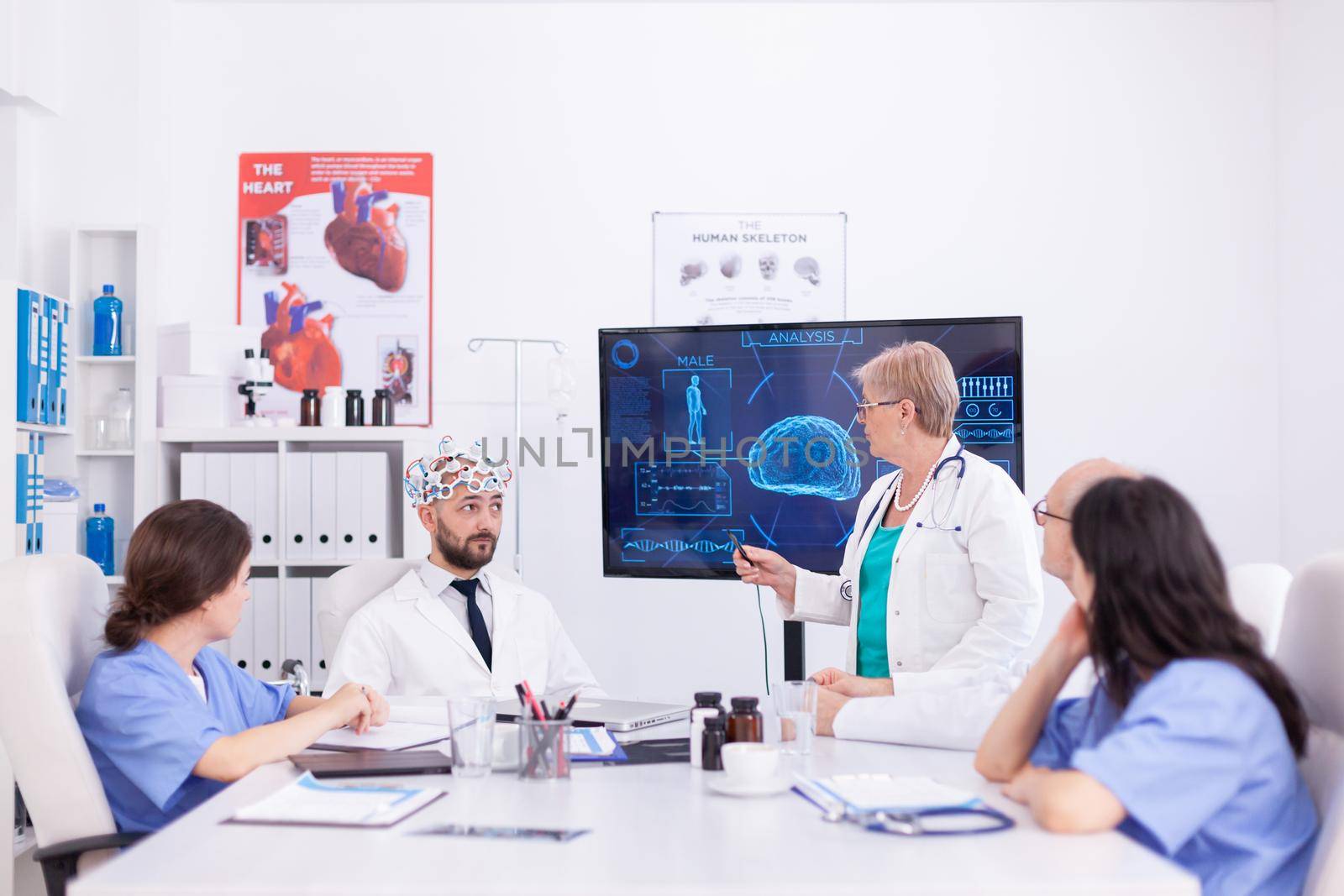 Consciousness doctor wearing headset with sensors for brain waves during neuoroscience, Monitor shows modern brain study while team of scientist adjusts the device.