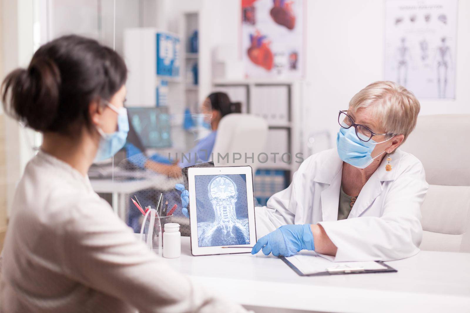 Doctor with face mask agasint covid-19 pointing at tablet pc with brain x-ray during consultation with patient.