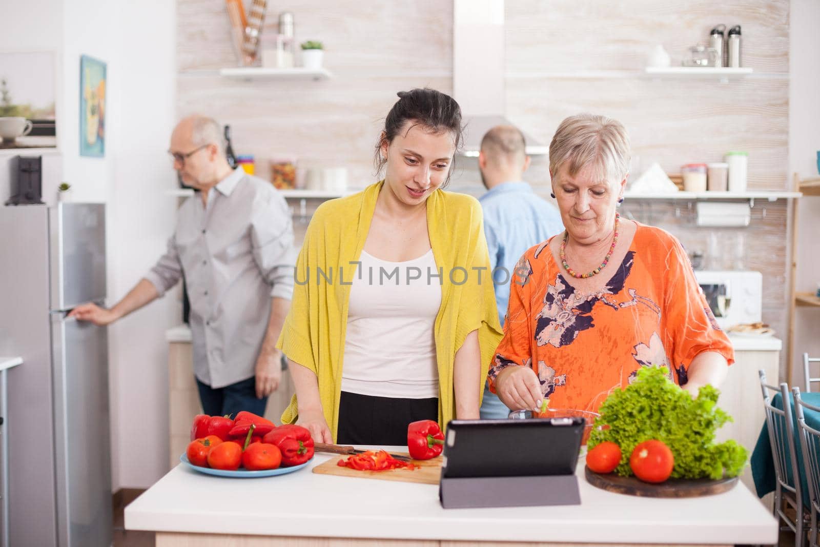 Mother and daughter checking recipe for vegetables salad on tablet pc in kitchen.