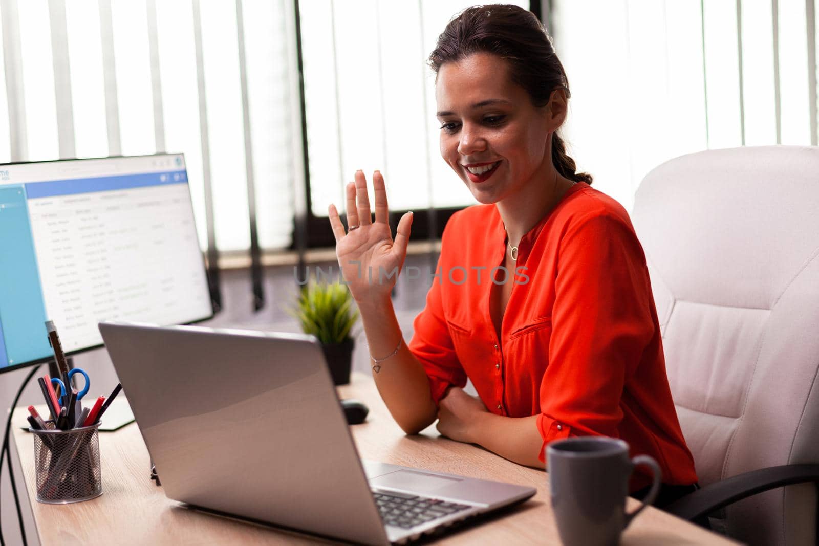 Businesswoman executive in video conference wave at team looking at camera. Entrepreneur using internet connection for video meeting with coworkers looking at webcam.