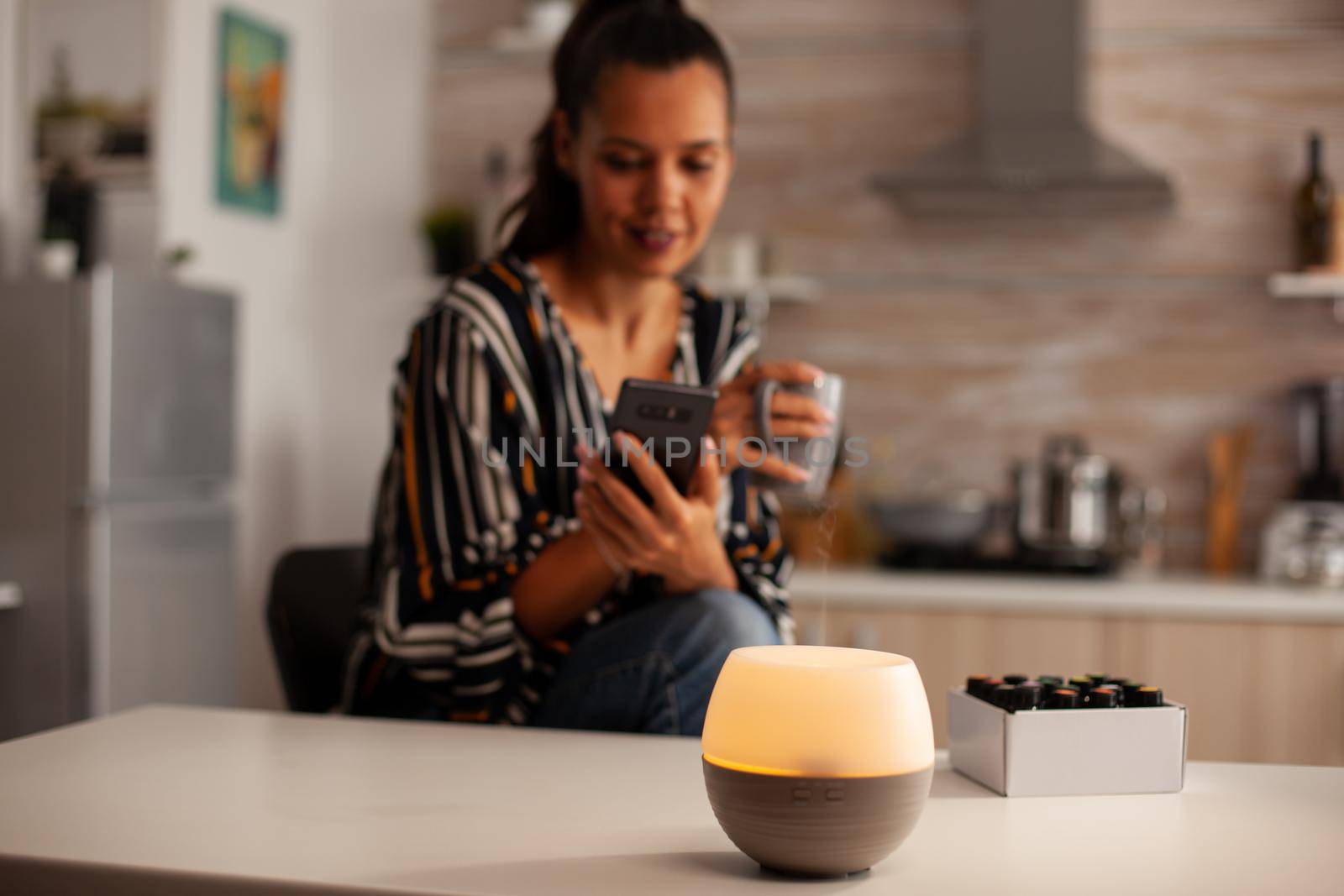 Woman watching video on phone and enjoying steam with essential oils from diffuser. Aroma health essence, welness aromatherapy home spa fragrance tranquil theraphy, therapeutic steam, mental health treatment
