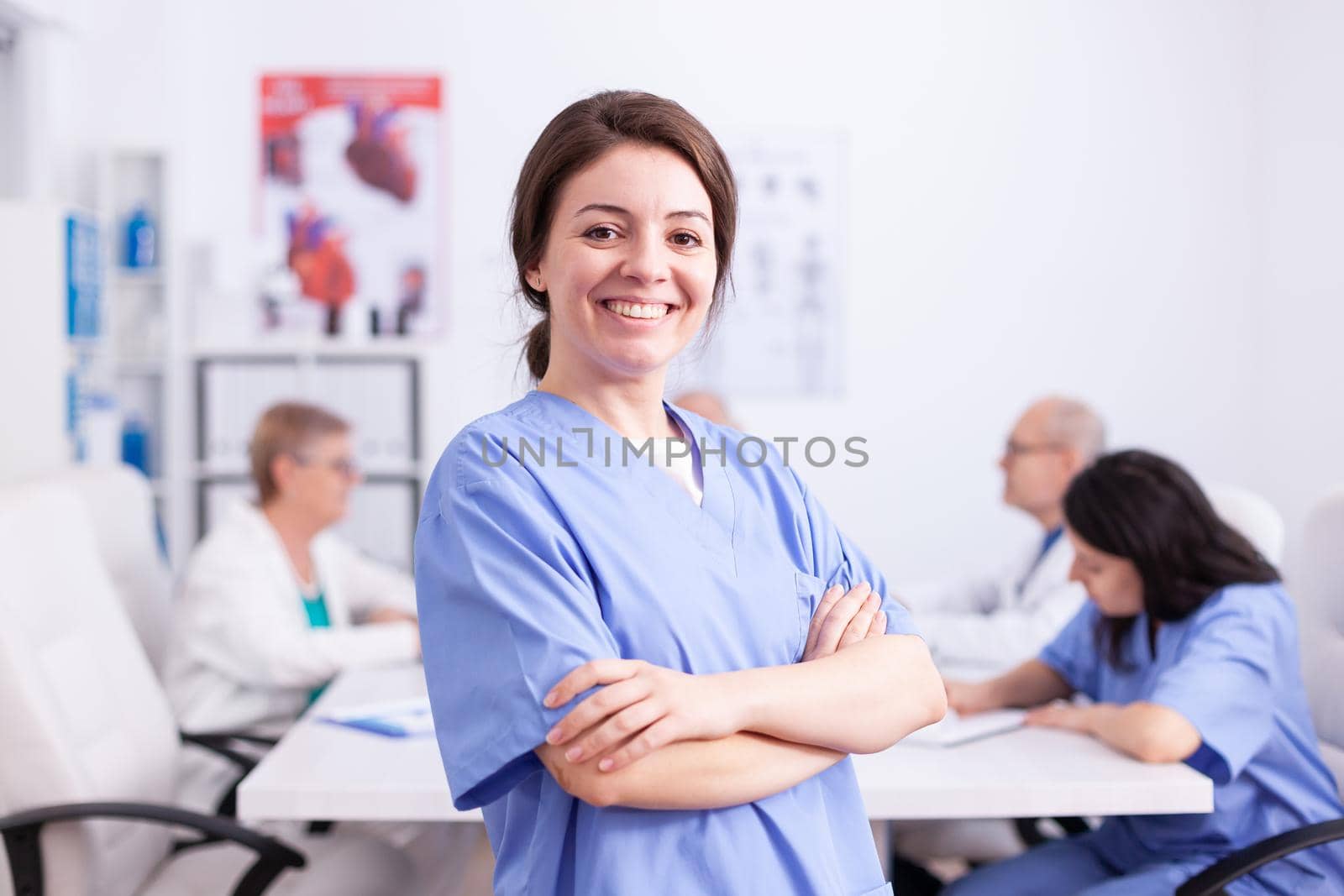 Young nurse wearing medical uniform in hospital conference room smiling at camera. Friendly medical practitioner in clinic meeting room, robe, specialist.