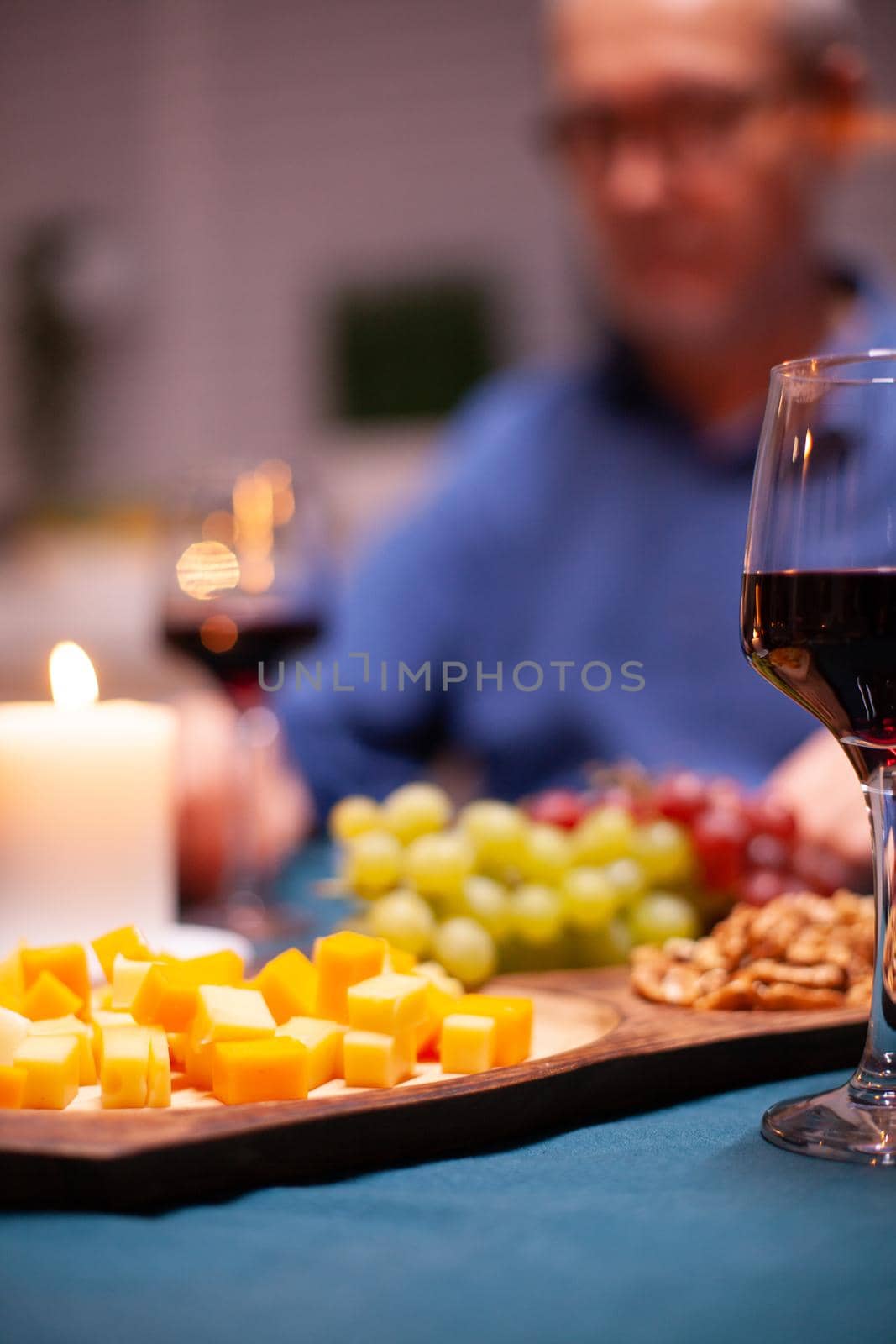 Grapes on wooden plate on kitchen table during festive dinner. Senior couple sitting at the table in kitchen, talking, enjoying the meal, celebrating their anniversary in the dining room.