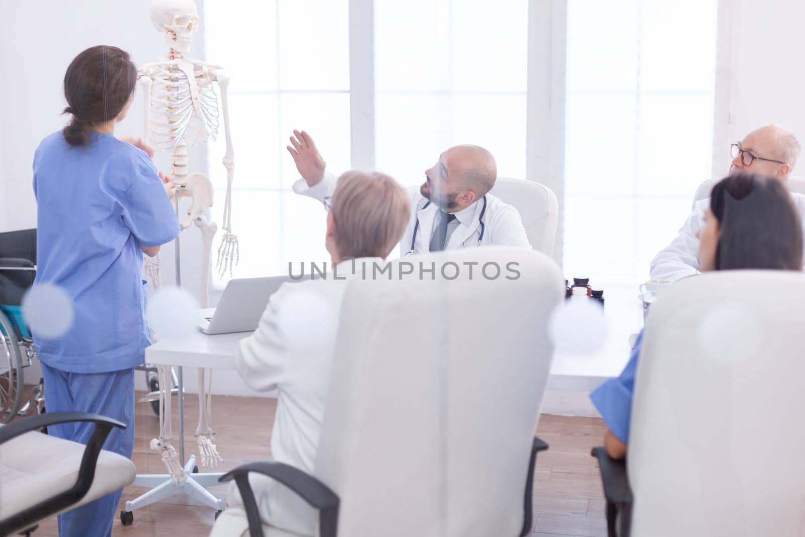 Expert doctor in radiology pointing at human skeleton during presentation in hospital conference room. Clinic therapist talking with colleagues about disease, medicine professional.