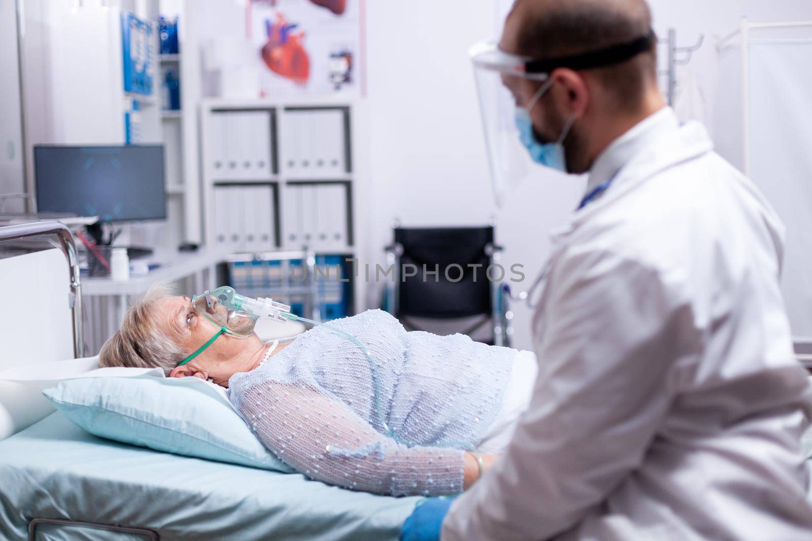 Woman can't breath without oxygen mask while laying in hospital and doctor sitting next to her wearing protection mask against coronavirus as safety precaution. Medical lungs infection treatment