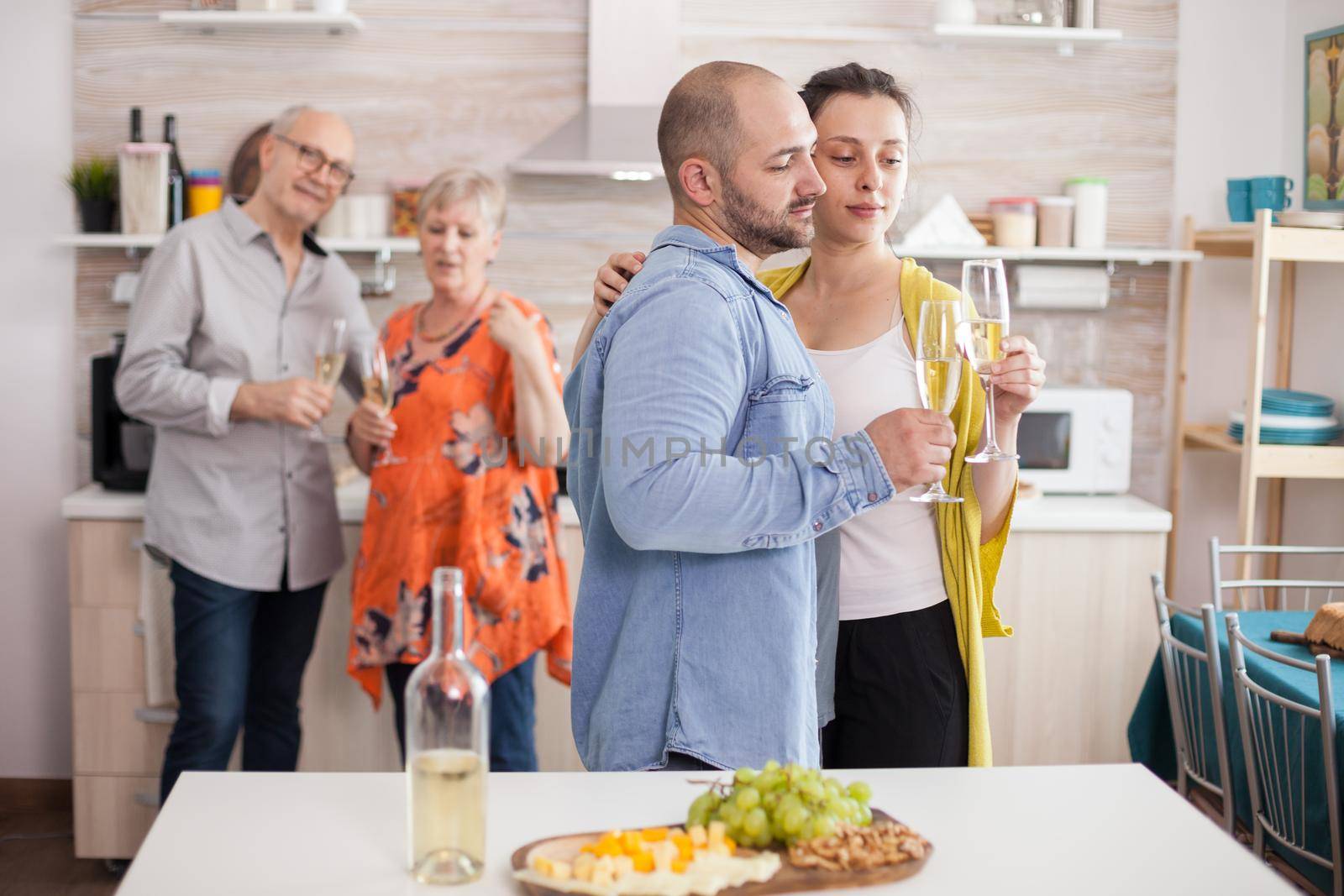 Couple holding and looking at glasses of wine in kitchen during brunch with family. Senior mother and father looking at son and his wife.