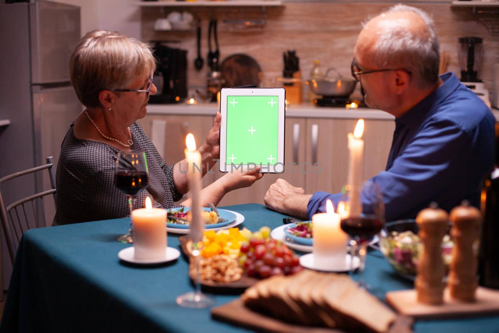 Green screen tablet at dinner. Aged people looking at green screen template chroma key display sitting at the table in kitchen during dinner.