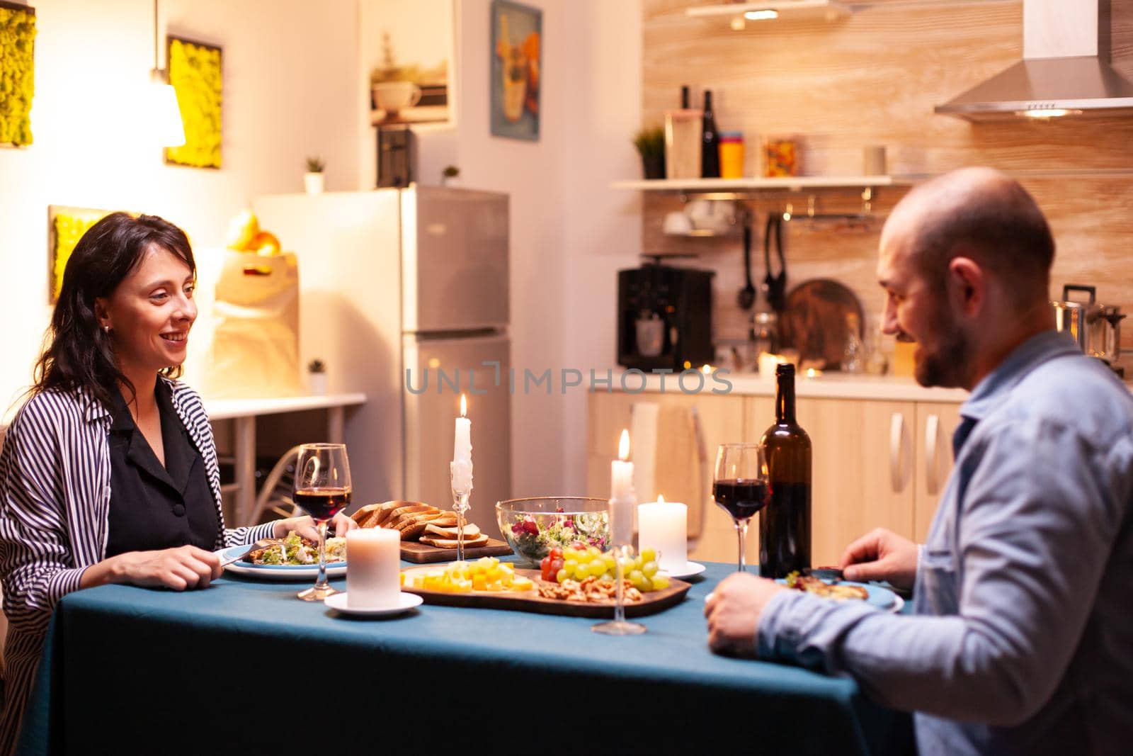 Boyfriend and girlfriend enjoying romantic dinner. Talking happy sitting at table dining room, enjoying the meal at home having romantic time at candle lights.