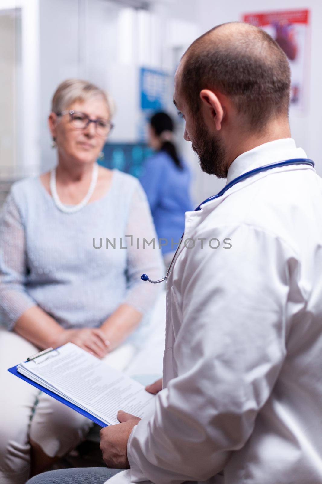 Doctor holding medical document while speaking with senior old woman in clinic cabinet. Converstation with medical stuff clinic medicine healthcare, senior, coat, clipboard.