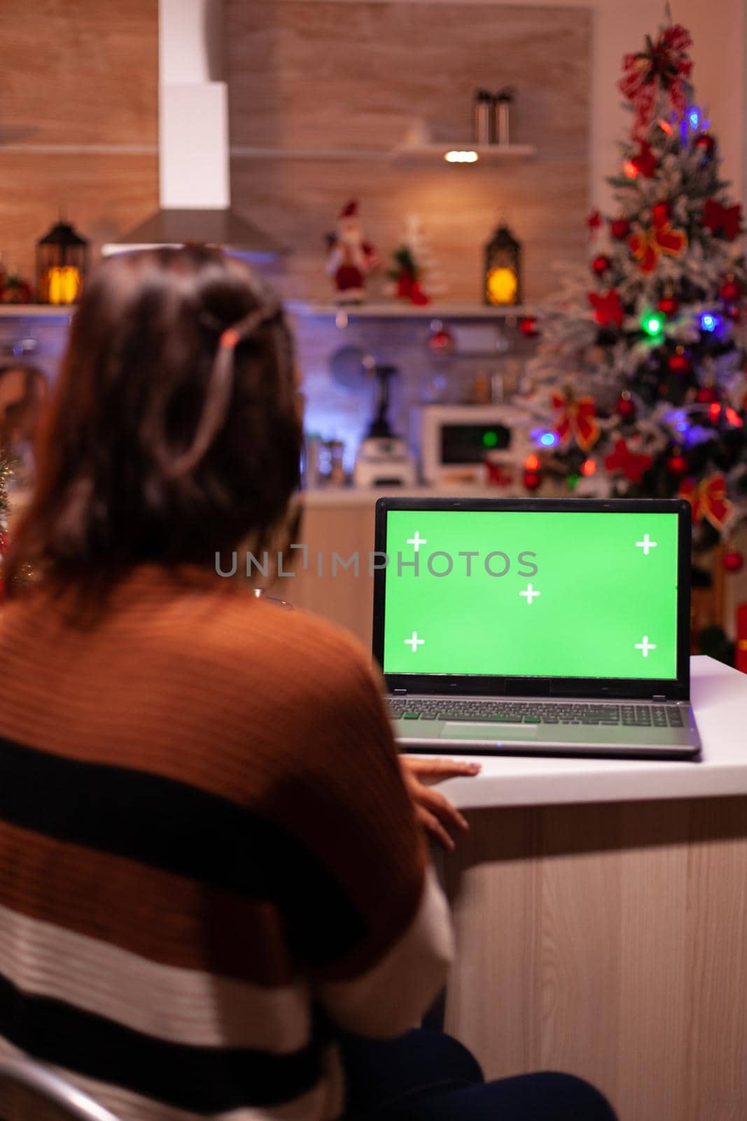 Caucasian young woman looking at green screen on laptop digital device sitting at festive home. Adult using modern chroma key notebook gadget on background display for mockup template