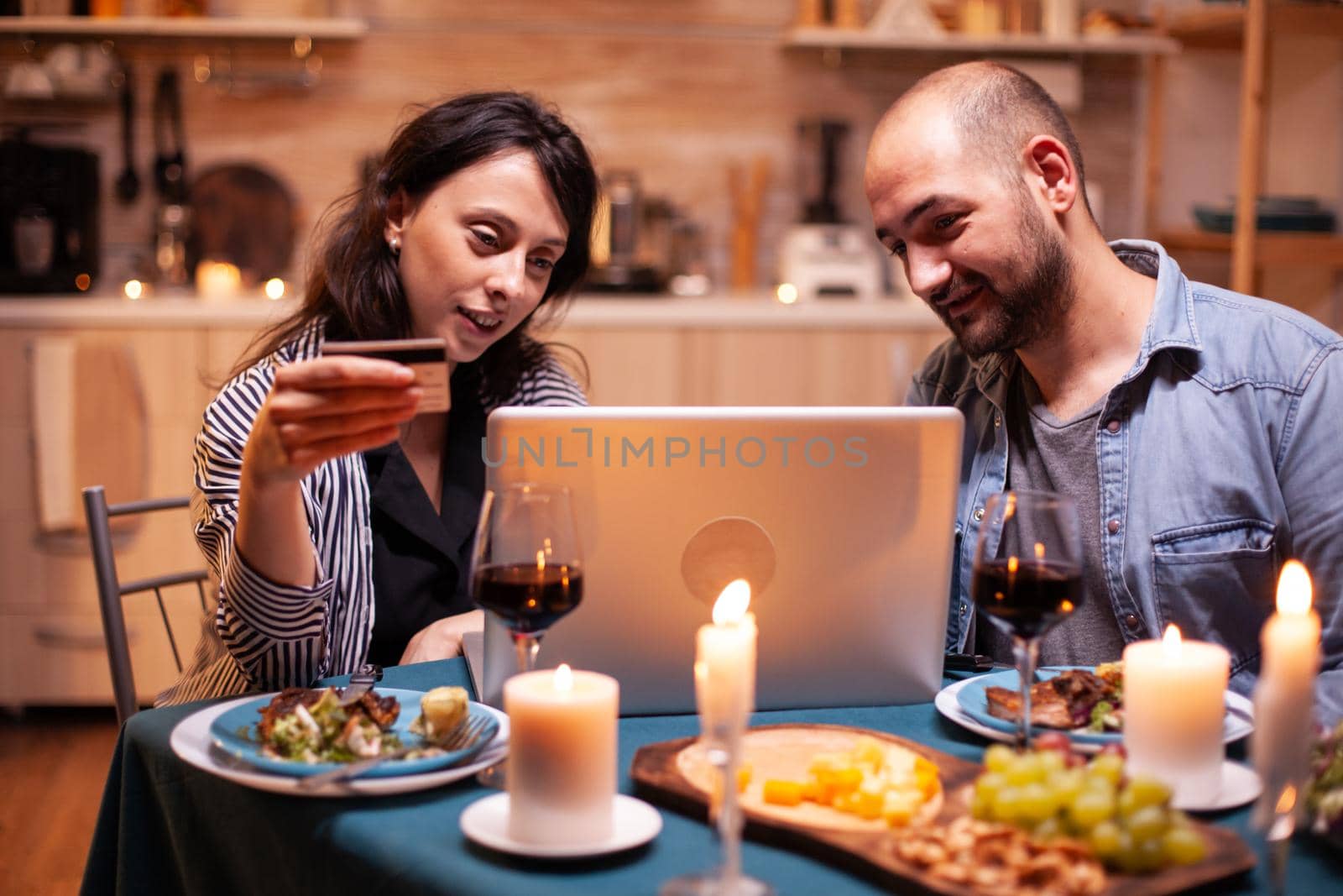 Couple doing shopping online at dinner on laptop. Adults sitting at the table, searching, browsing, surfing, using technology card payment, internet