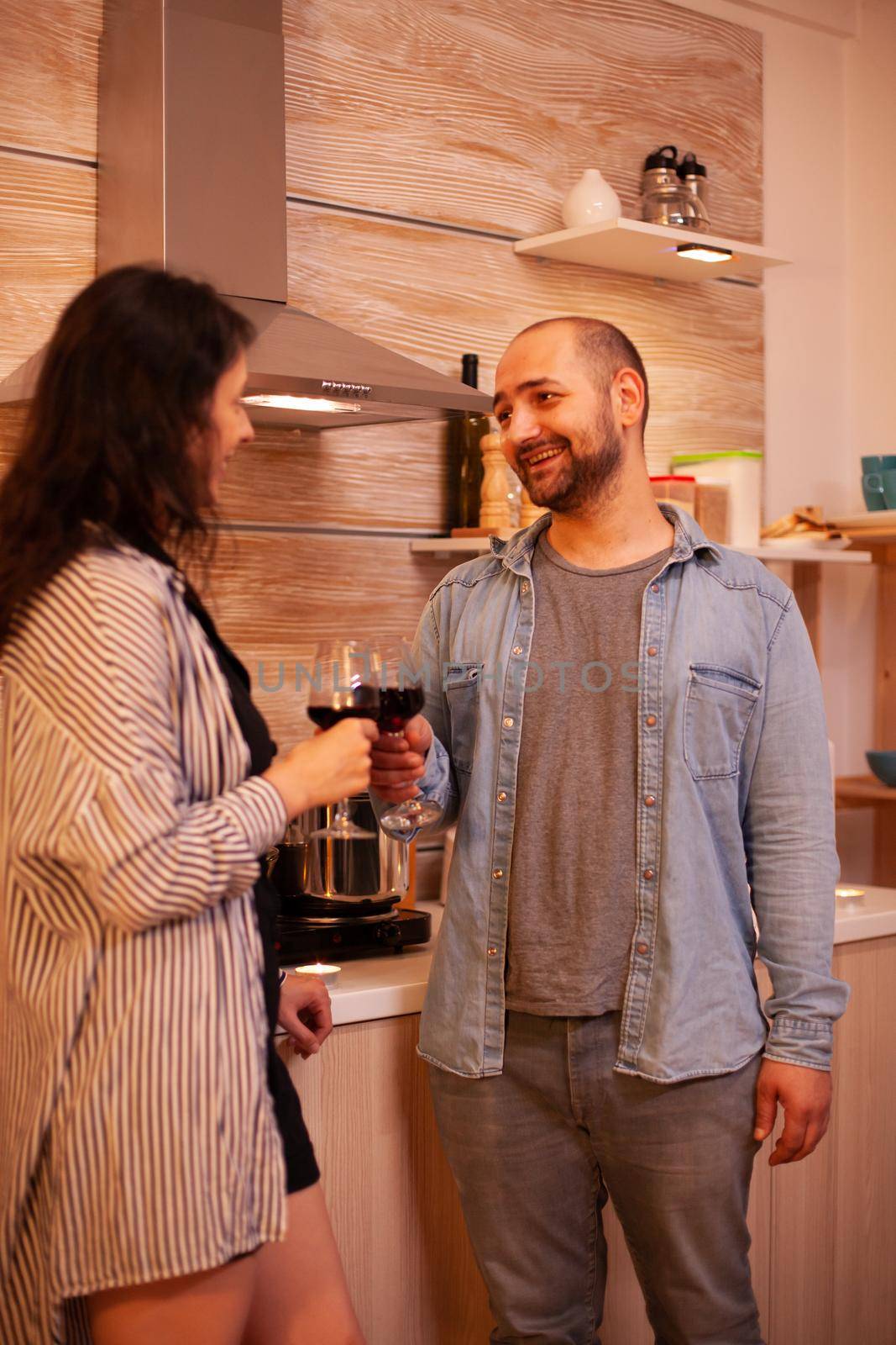 Young beautiful woman flirting with man during date. Adult couple having romantic date at home, in the kitchen, drinking red wine, talking, smiling, enjoying the meal in dining room.