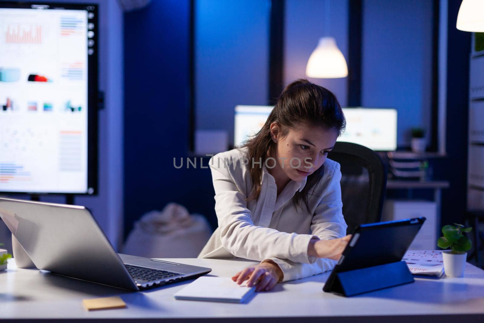 Manager woman using laptop and tablet in same time working on financial reports in business start-up office . Busy multitasking employee using modern technology network wireless late at night