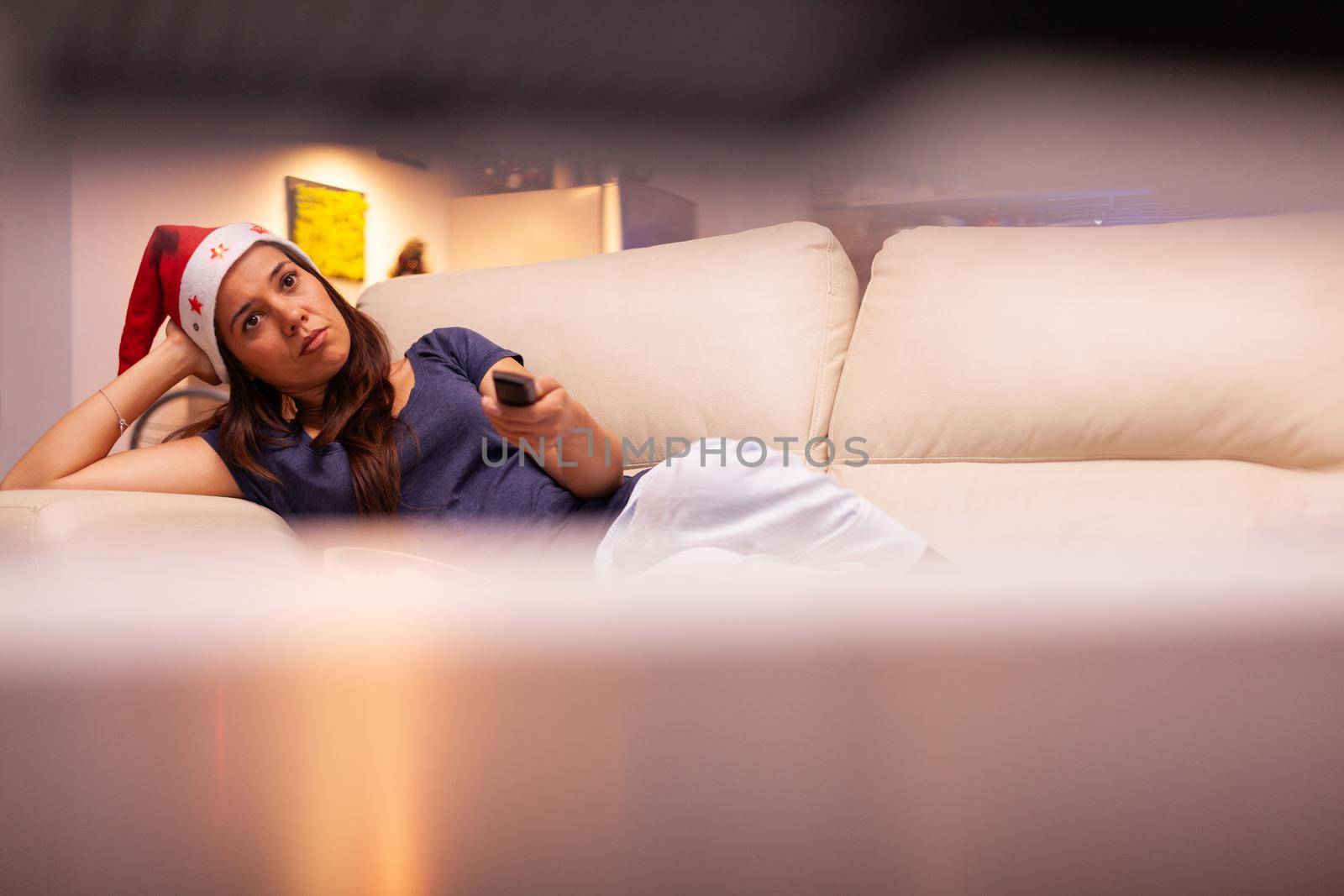 Girl lying on couch changing channel using remote control by DCStudio