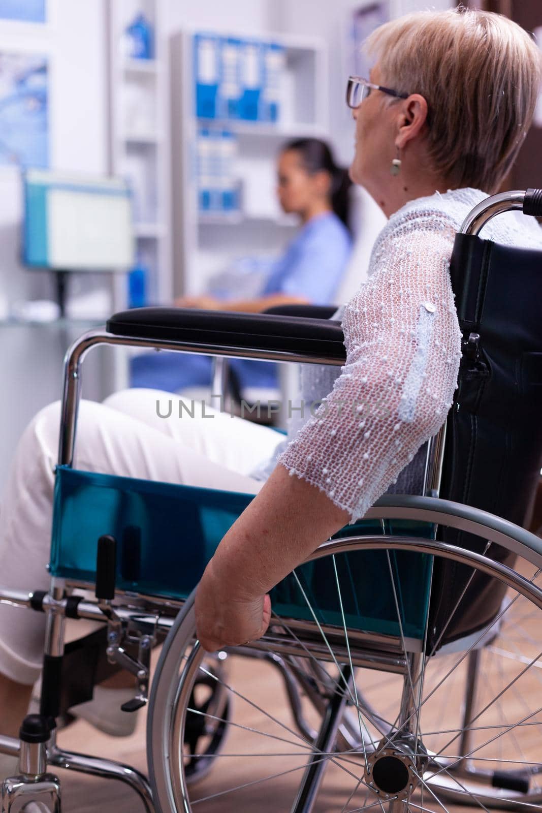 Handicapped senior woman in wheelchair during consultation in hospital hallway.