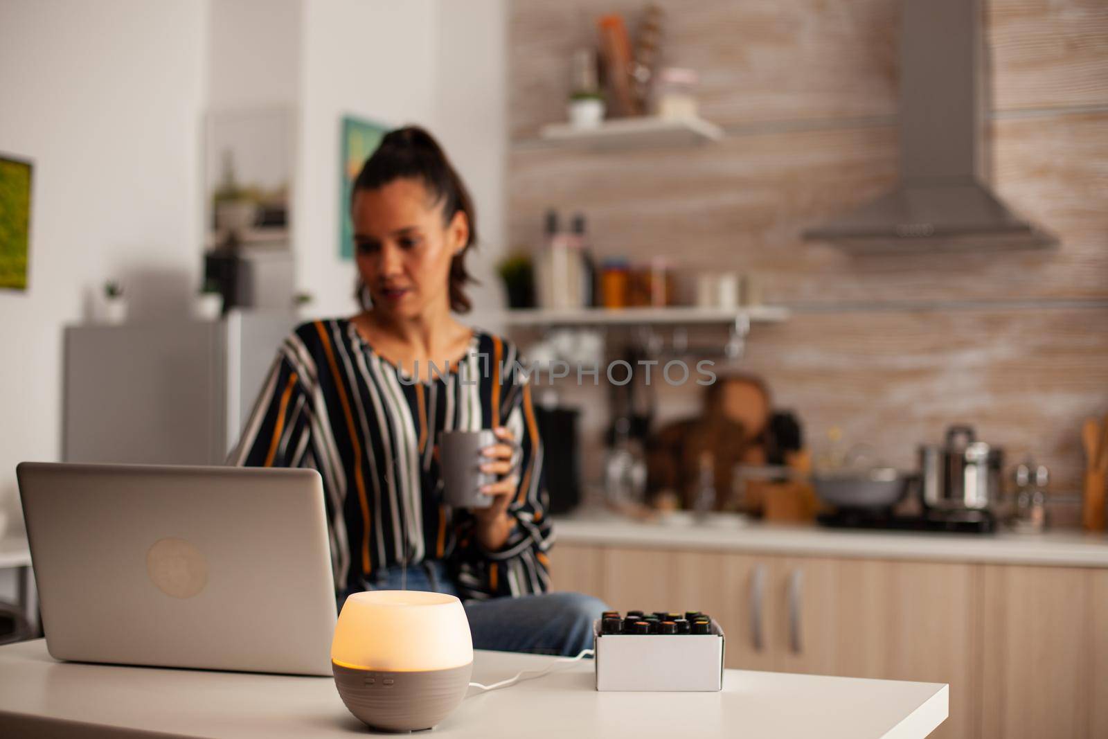 Woman surfing on laptop and diffuser wtih essential oils. Aroma health essence, welness aromatherapy home spa fragrance tranquil theraphy, therapeutic steam, mental health treatment