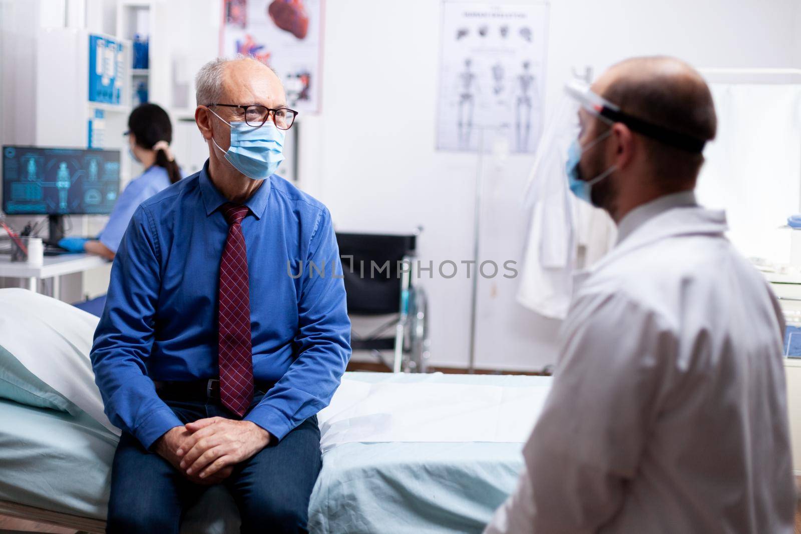 Doctor talking with senior woman wearing face mask about protection against coronavirus pandemic. Global health crisis, medical system during pandemic, sick elderly patient in private clinic.