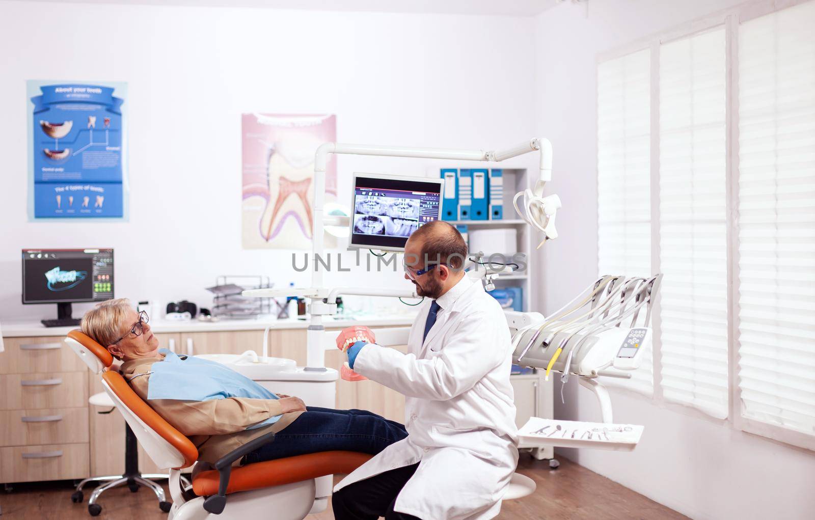 Dentist explaining oral hygiene holding model of cavity during consultation of senior woman. Medical teeth care taker discussing with senior woman about mouth hygiene.