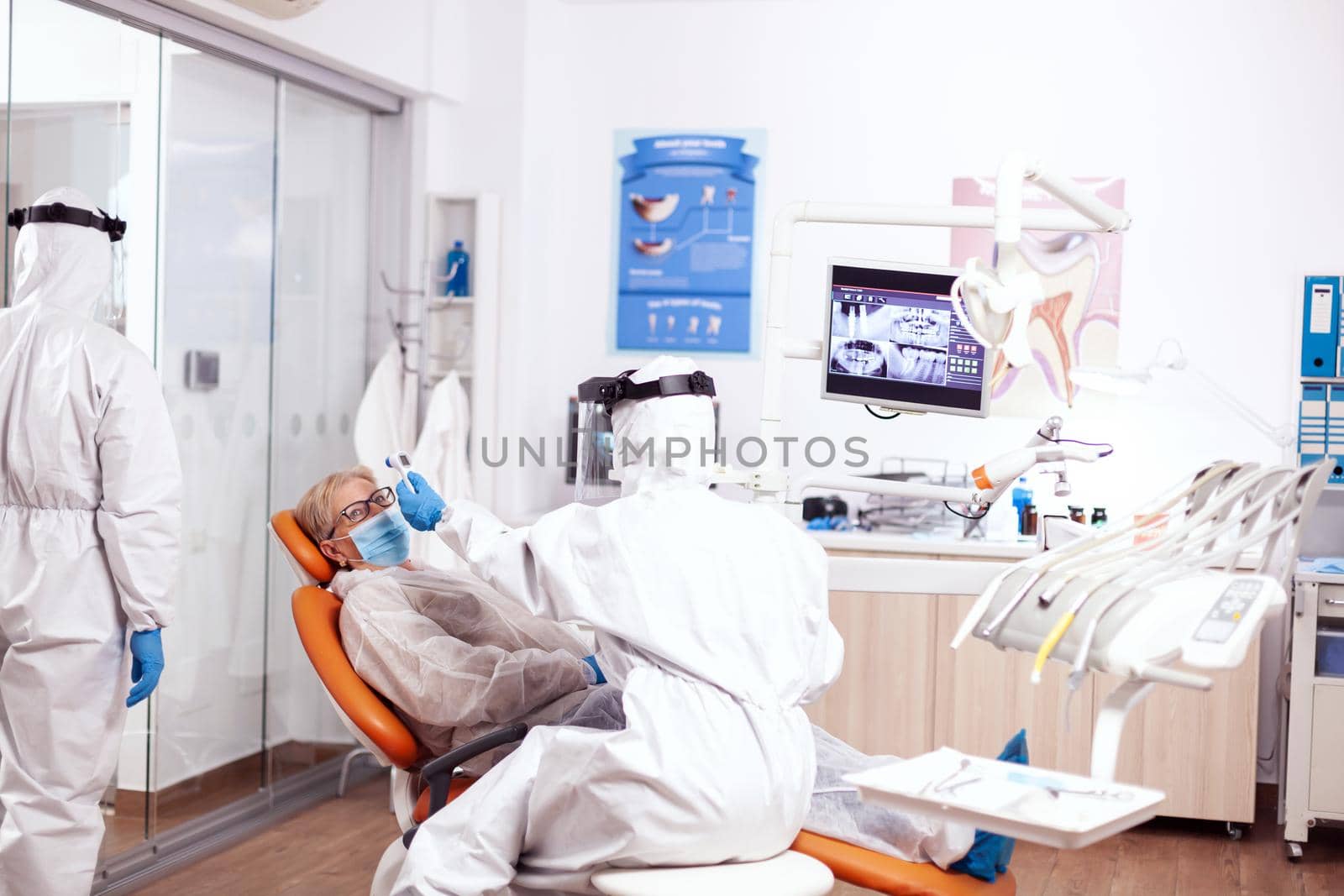 Dentist nurse taking patient temperature wearing hazmat suit by DCStudio