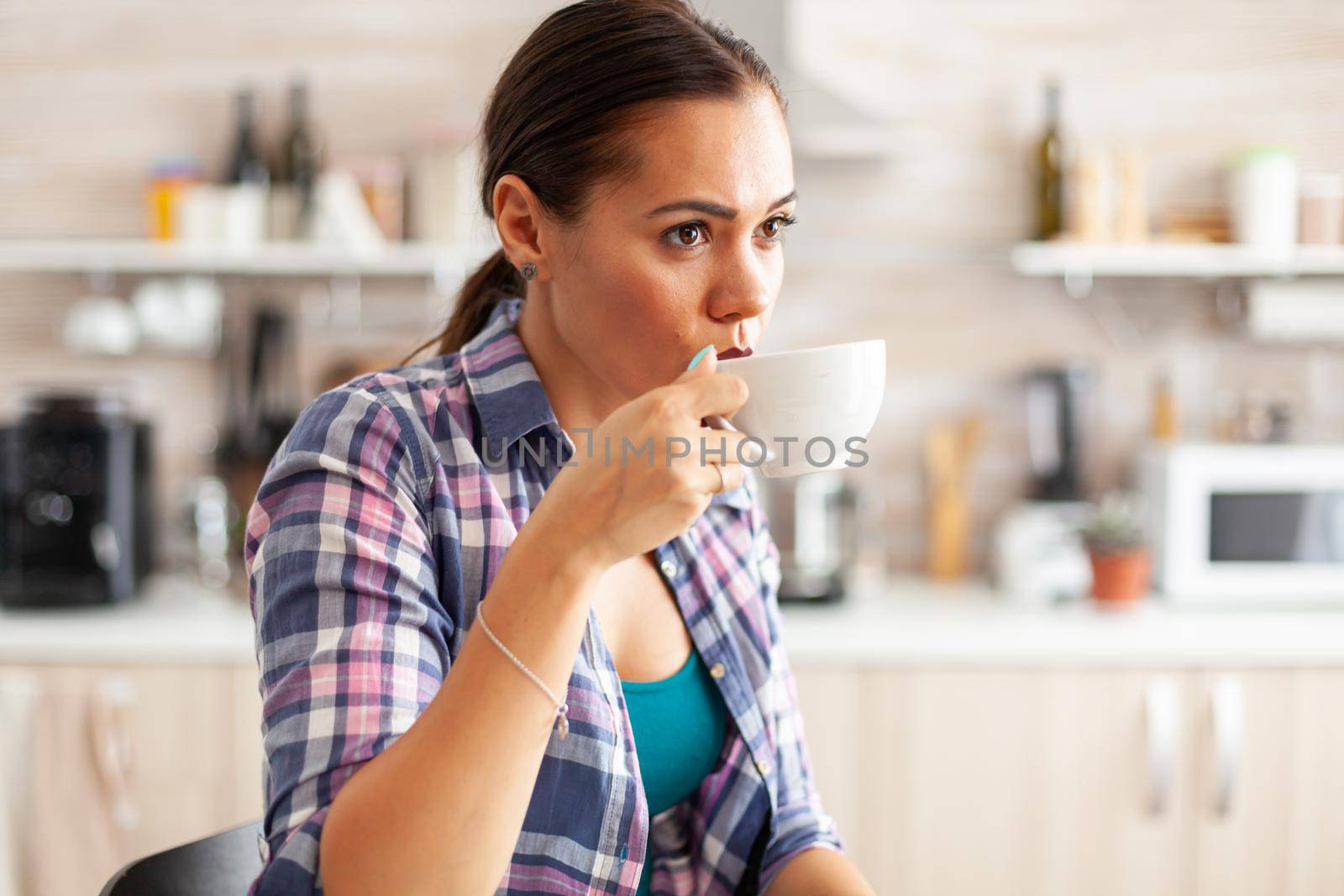 Lady relaxing and sipping hot green tea from porcelain cup during breakfast in Pretty lady sitting in the kitchen in the morning during breakfast time relaxing with tasty natural herbal tea.