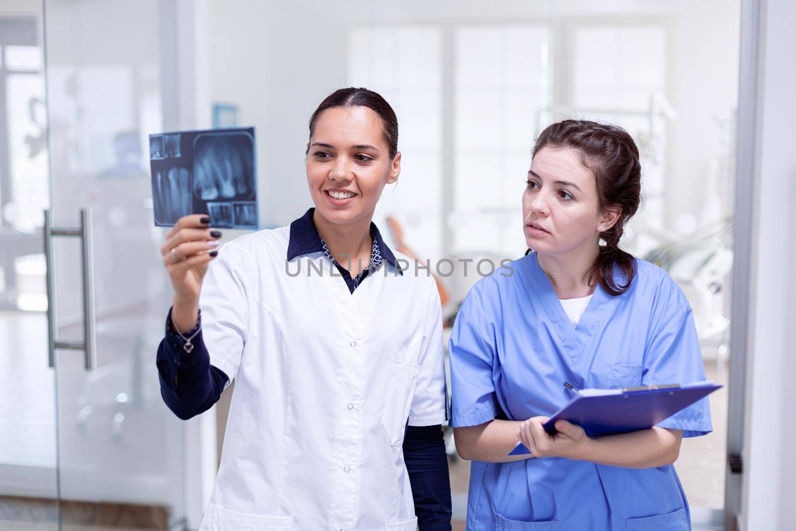 Dentist doctor holding teeth x-ray and nurse taking notes by DCStudio