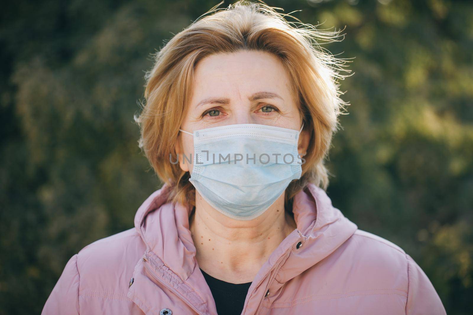 Woman in Medical Mask. Breathes deeply and looking at camera on green background outdoor. Health care and medical concept