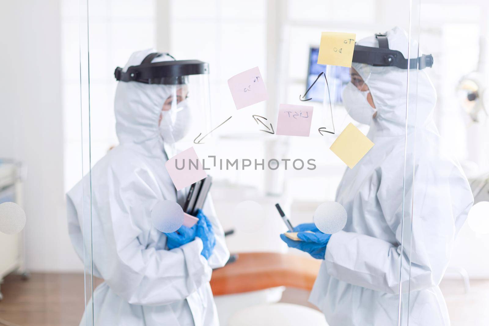 Tired dentist discussing about patient diagnosis wearing ppe suit by DCStudio