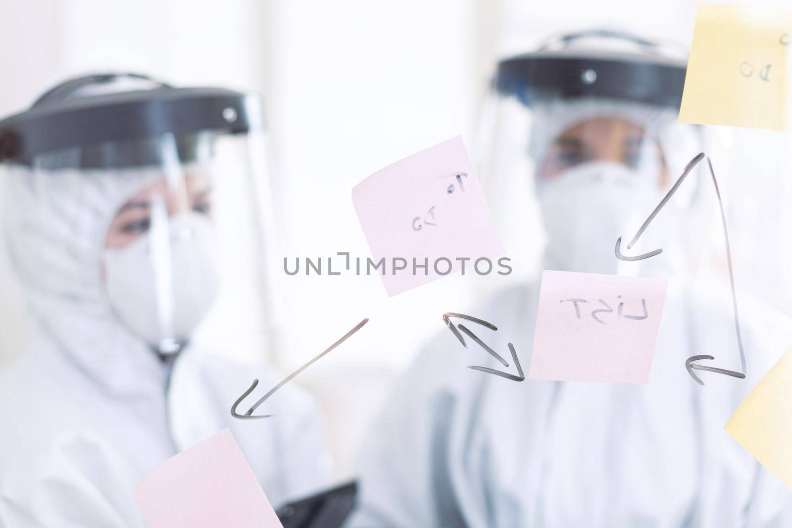 Stomatologs dressed in ppe suit during covid-19 as safety precaution. Medical team in stomatology office wearing coverall in dental office writing ideas on sticky notes.