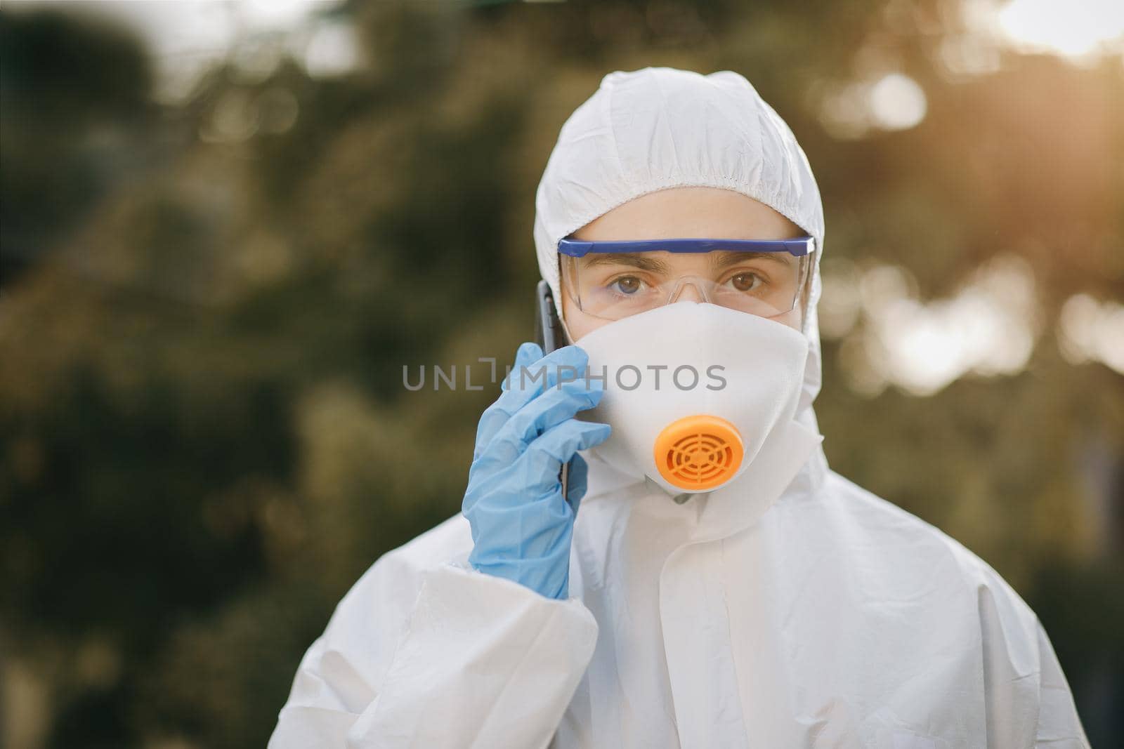 Medical worker portrait. Doctor epidemiologist fighting with coronavirus COVID-19. Confident Asian doctor in protective PPE suit talking on the phone. Girl in chemical protection suit