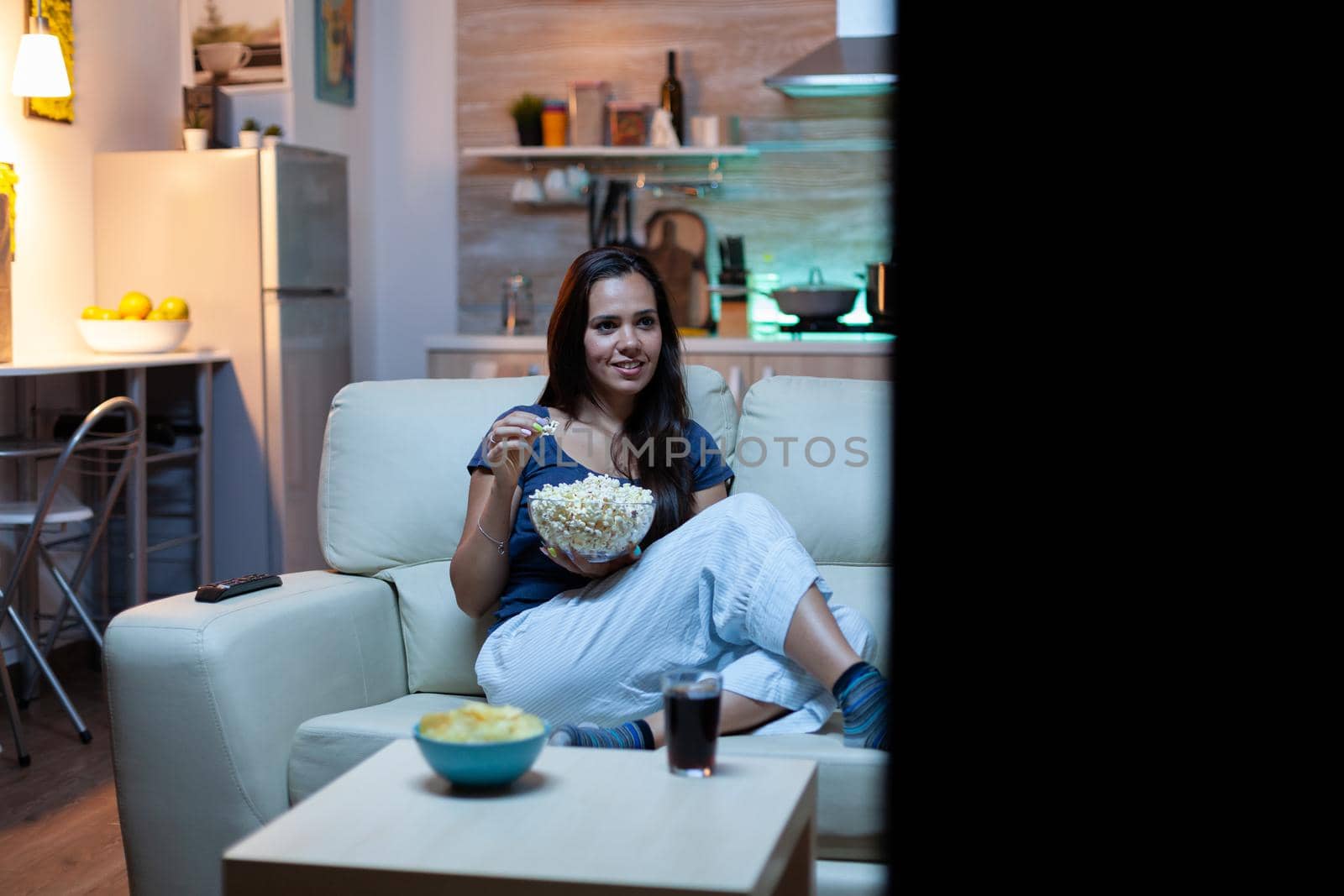 Woman eating popcorn on sofa by DCStudio