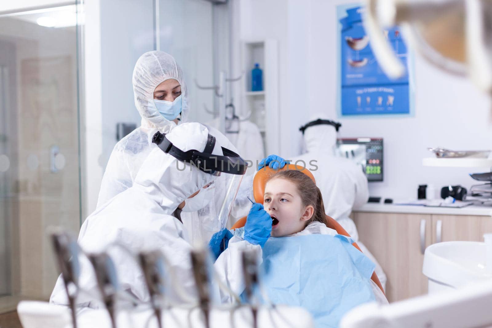 Dental specialist in ppe suit checking child cavity by DCStudio