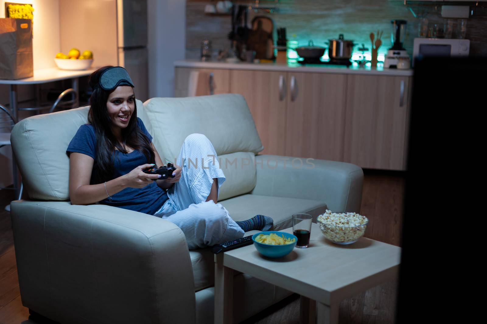 Determined woman playing video game in living room at night. Excited gamer woman sitting on couch, playing and winning video games using console and wireless controller.