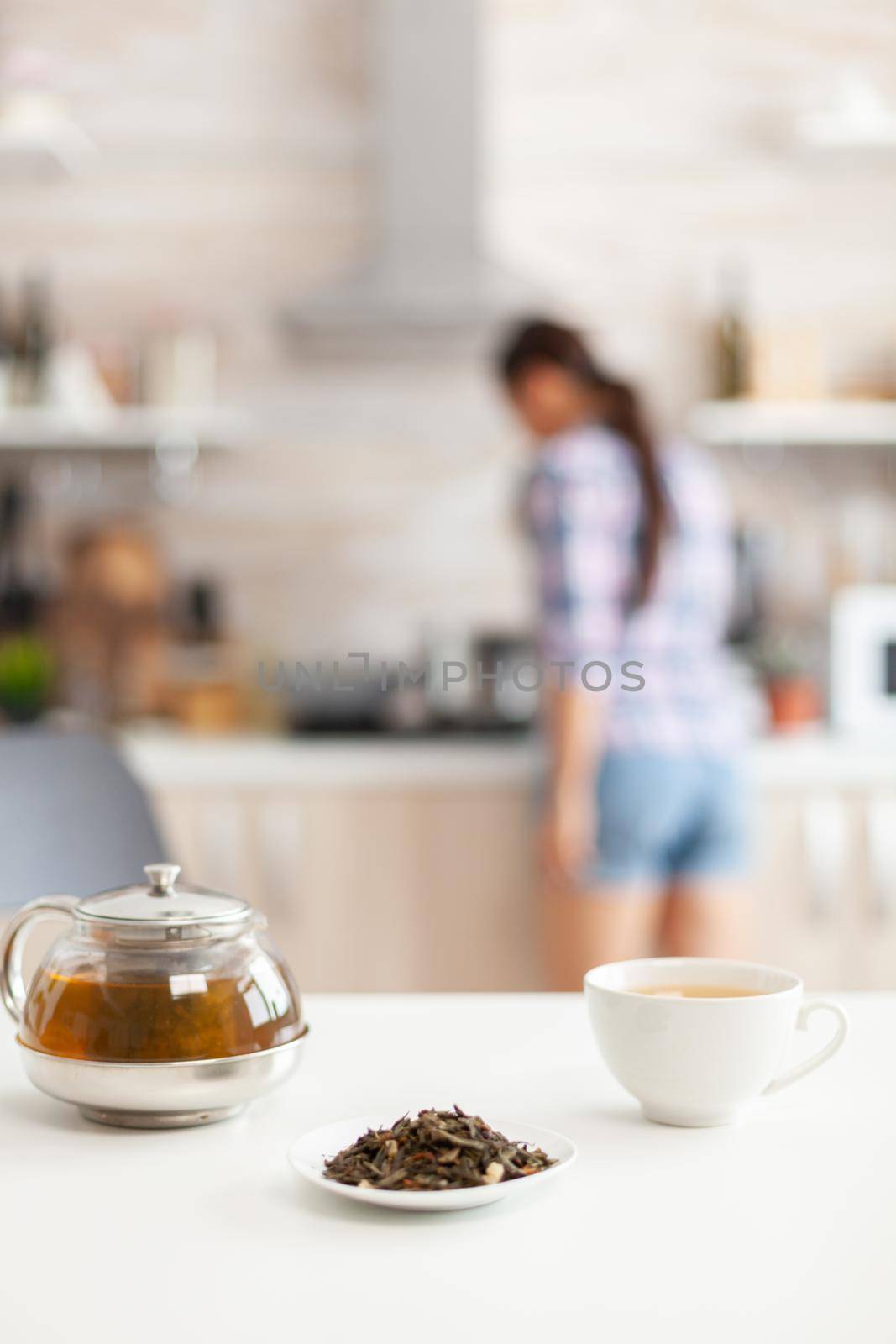 Woman preparing tasty food for breakfast in kitchen and using aromatic herbs for green tea. Shot with background blur of lady having great morning with tasty natural healthy herbal tea sitting in the kitchen.