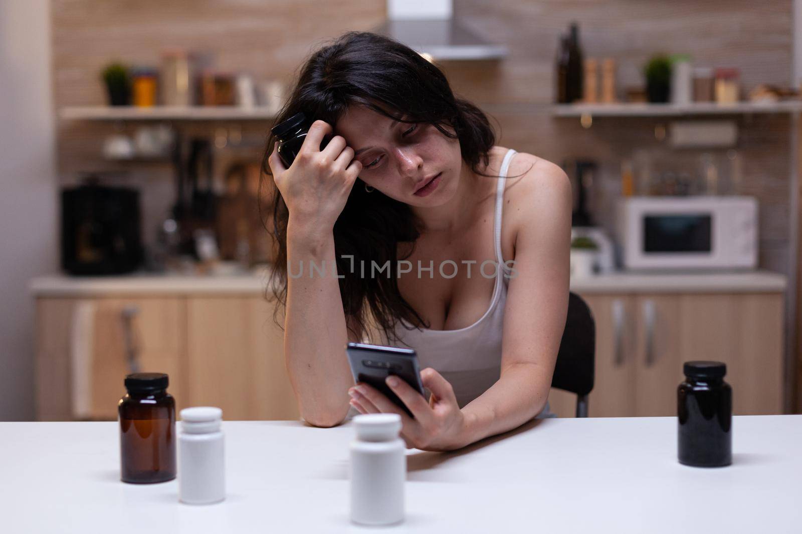 Portrait of woman with painful migraine holding bottle of medicine reading prescription for pills, drugs, remedy, medication, treatment and medicament on smartphone against headache