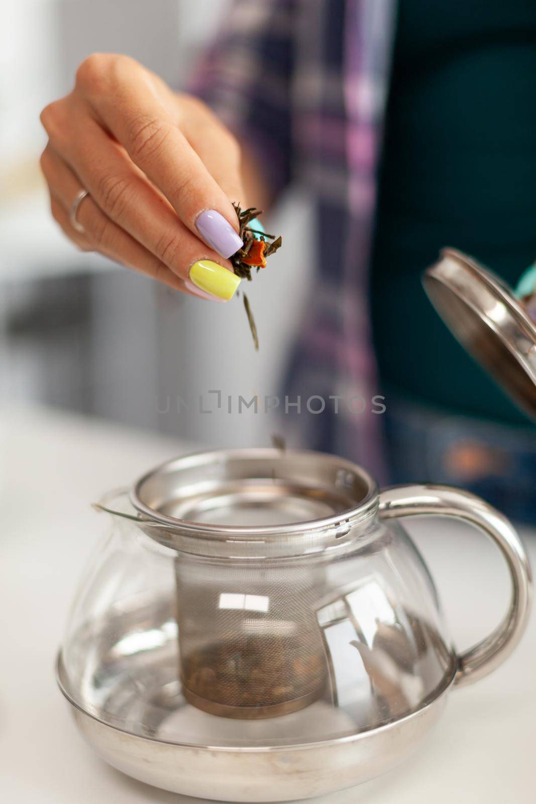 Close up of housewife brewing green tea during breakfast in kitchen. Preparing tea in the morning, in a modern kitchen sitting near the table. Putting with hands, healthy herbal in pot.