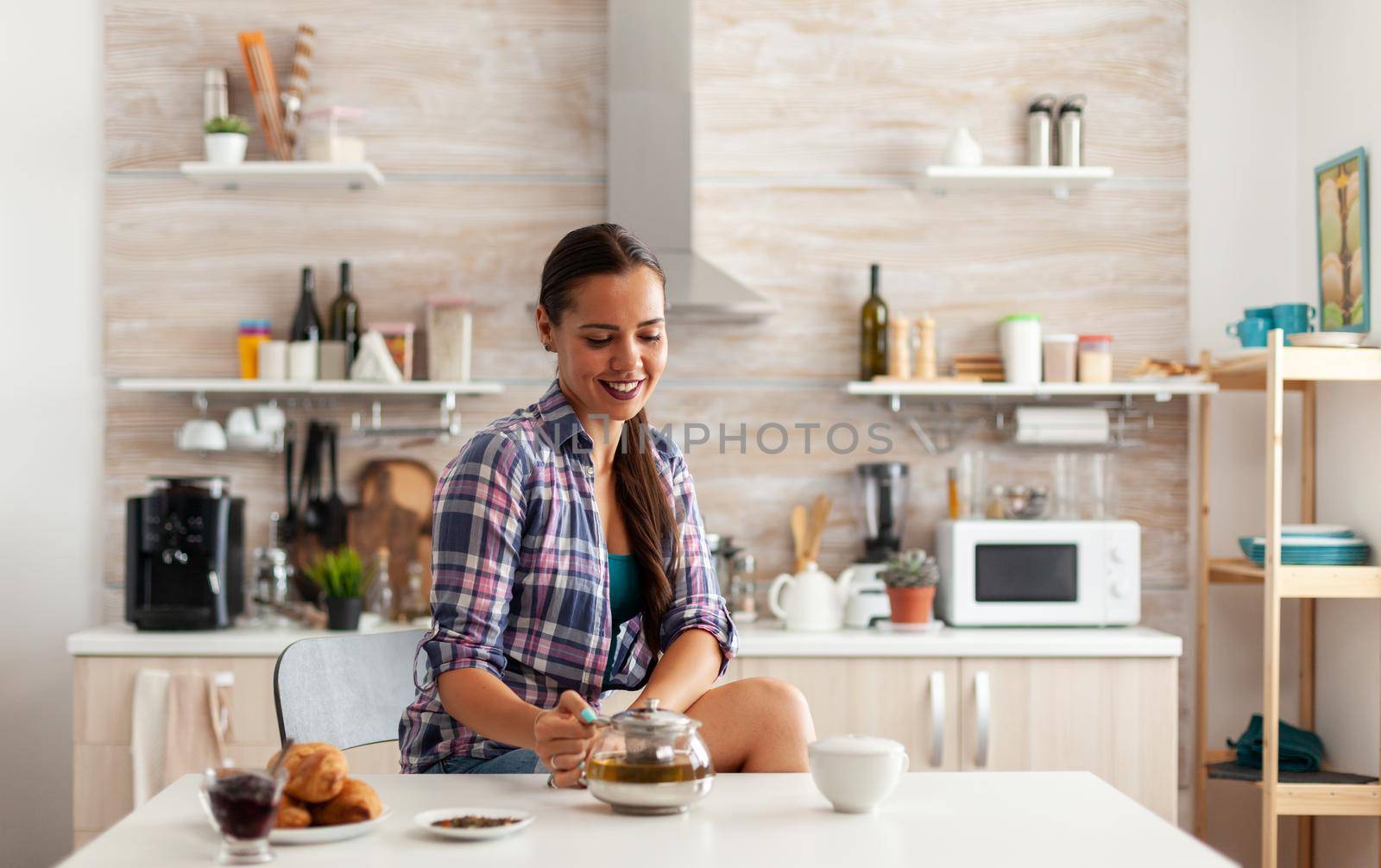 Young lady drinking green tea and smiling at breakfast sitting at the table in the kitchen. Woman, lifestylem, beverage, preparation, herbal, teapot, morning, aromatic.