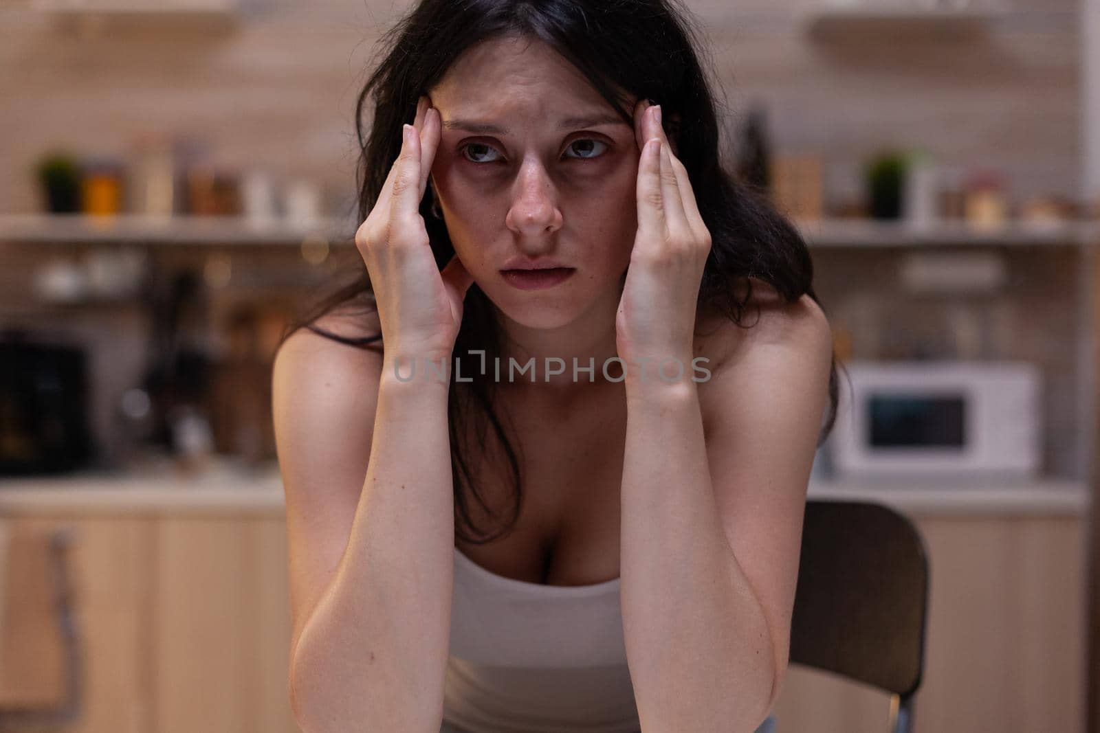 Portrait of stressed woman with headache at home, touching face and temples because of painful migraine and depression. Unhappy woman with tension and hurt from stress and fatigue